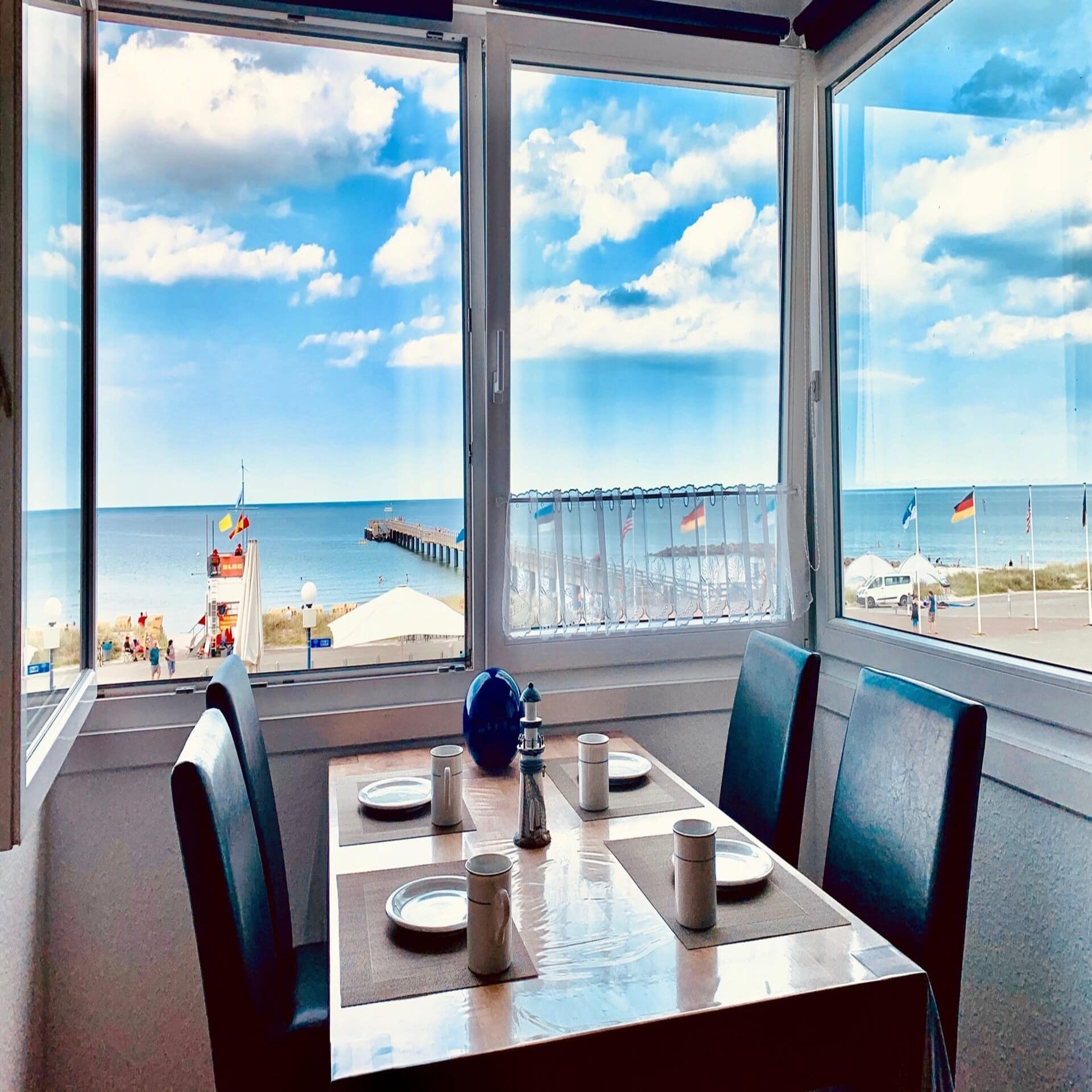 Tisch für 4 Personen am geöffneten Fenster mit Blick auf die Promenade, eine Seebrücke und das Meer.