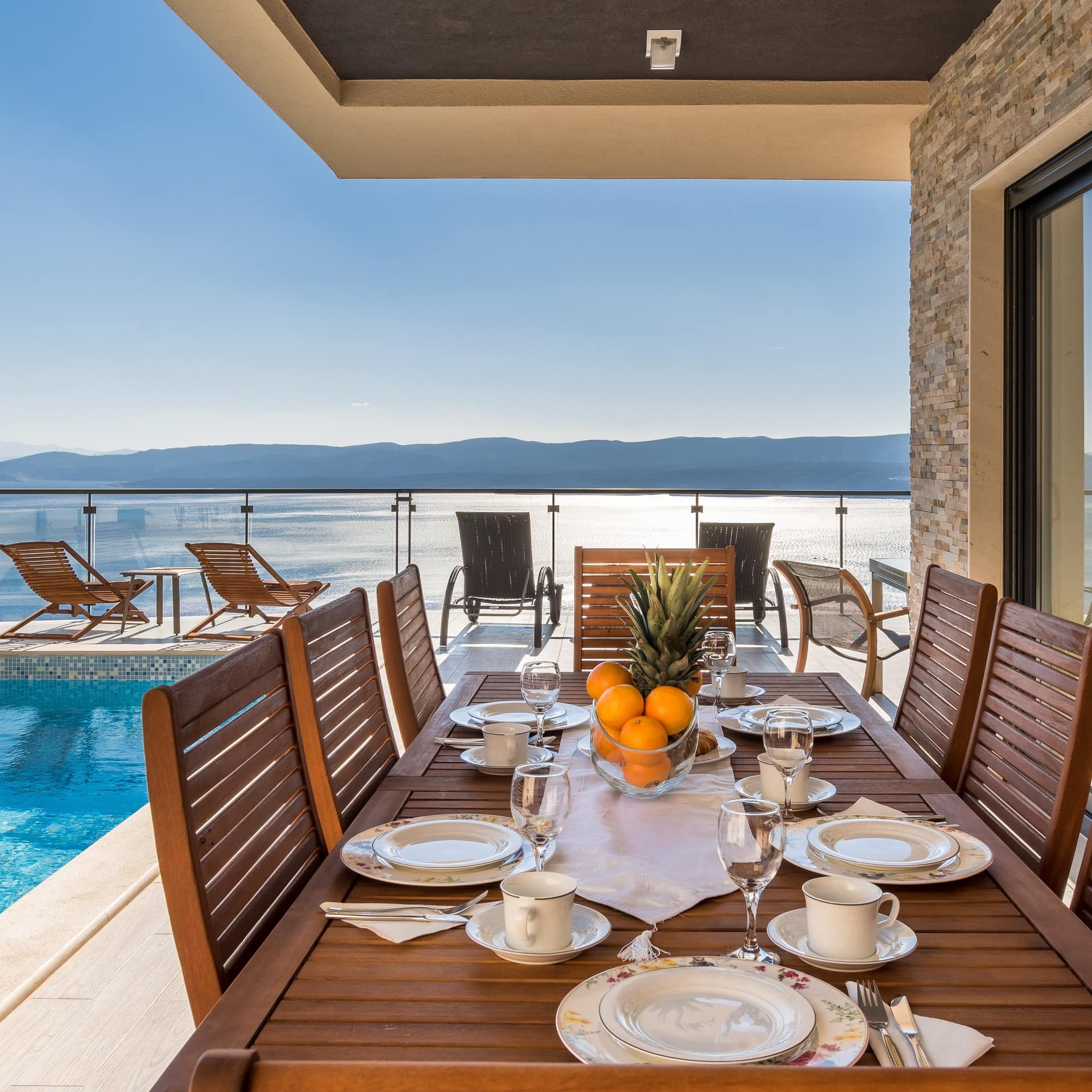 Gedeckter Frühstückstisch neben einem Außenpool mit Sonnenliegen in einem Ferienhaus in Kroatien mit Blick auf das Meer