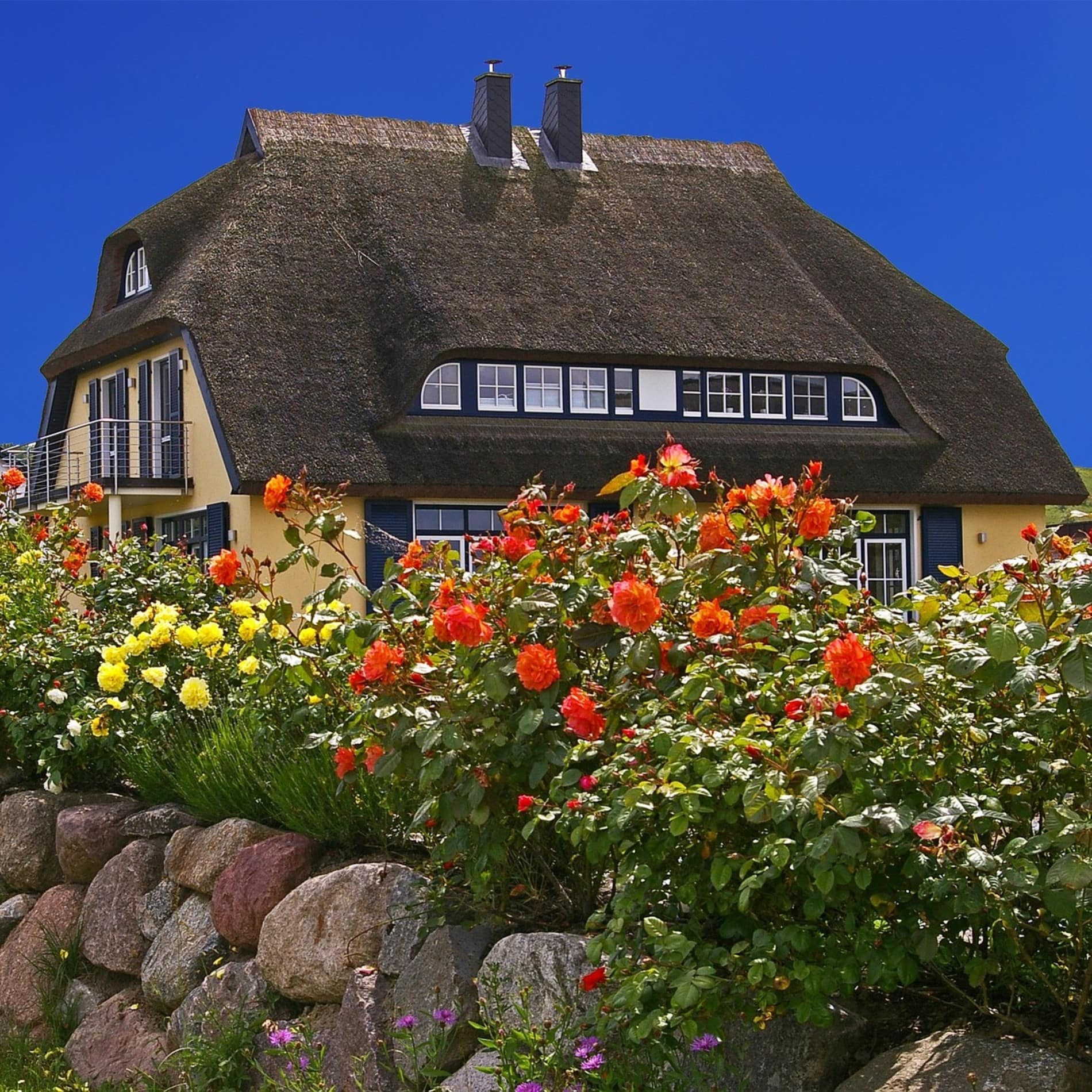 Bungalow in Norddeutschland mit Reetdach, Blumen und Steinmauer