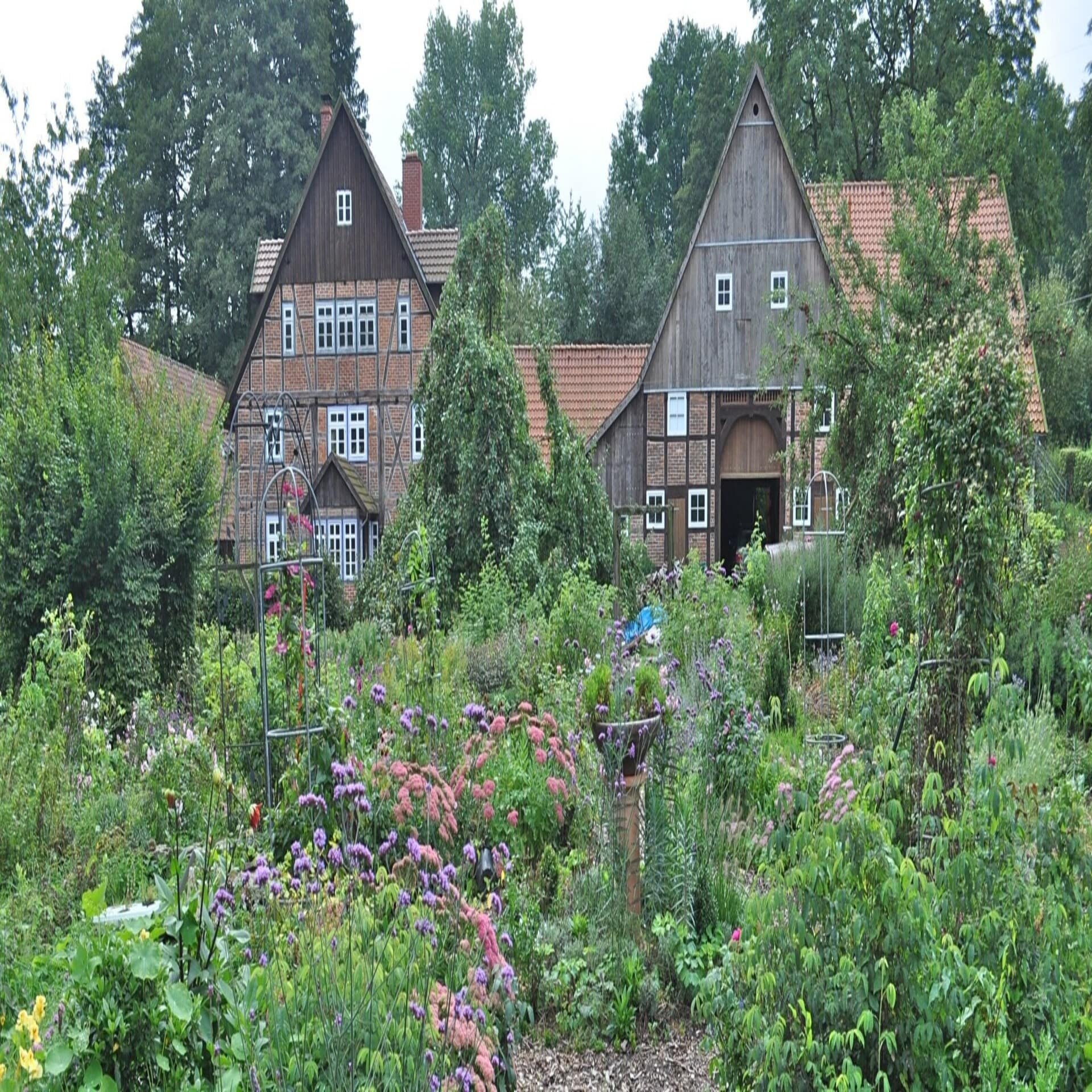 Blick über einen blühenden Nutzgarten auf einen alten Fachwerkbauernhof.