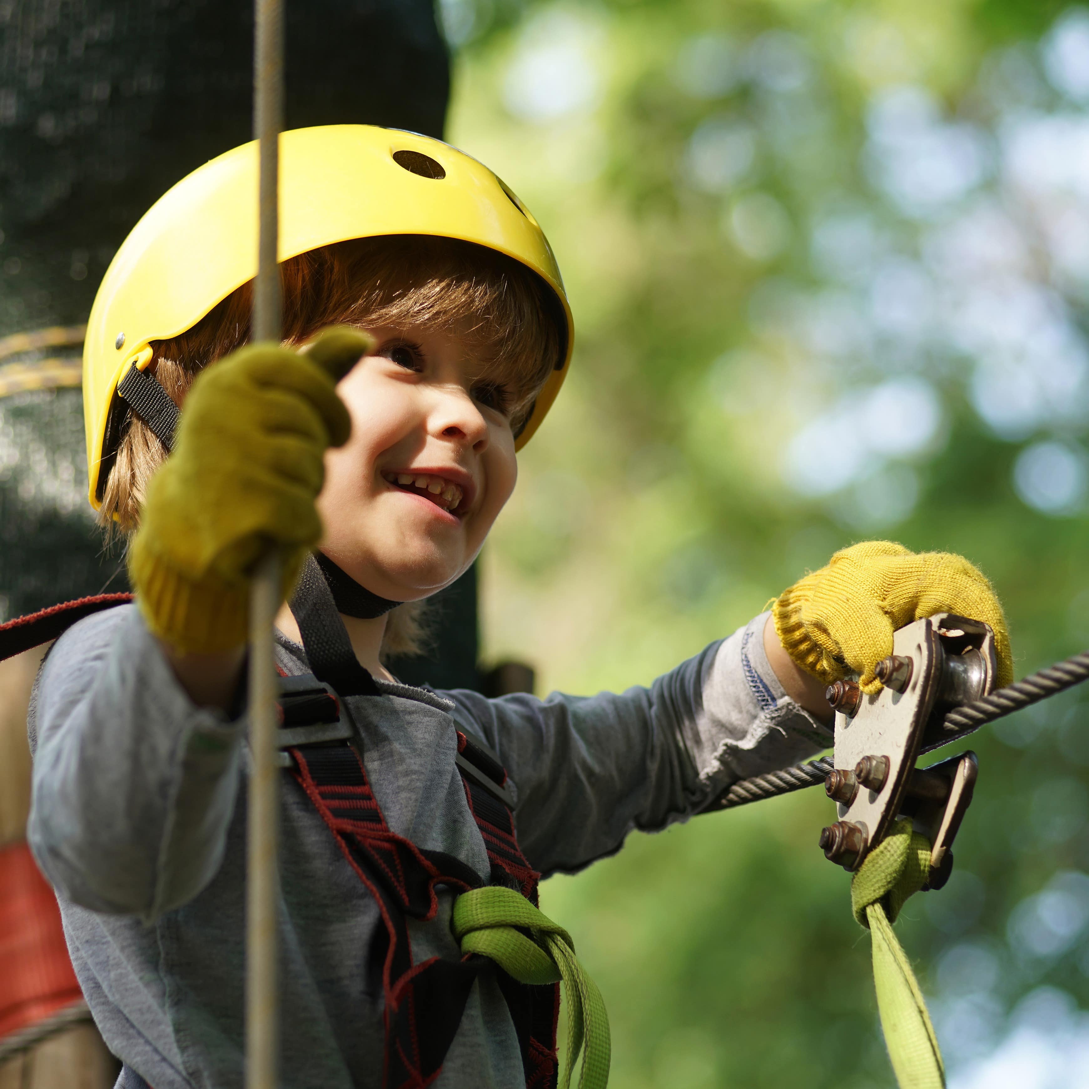 Nahaufnahme: Ein kleiner Junge mit gelbem Helm auf einem Kletterparcours.