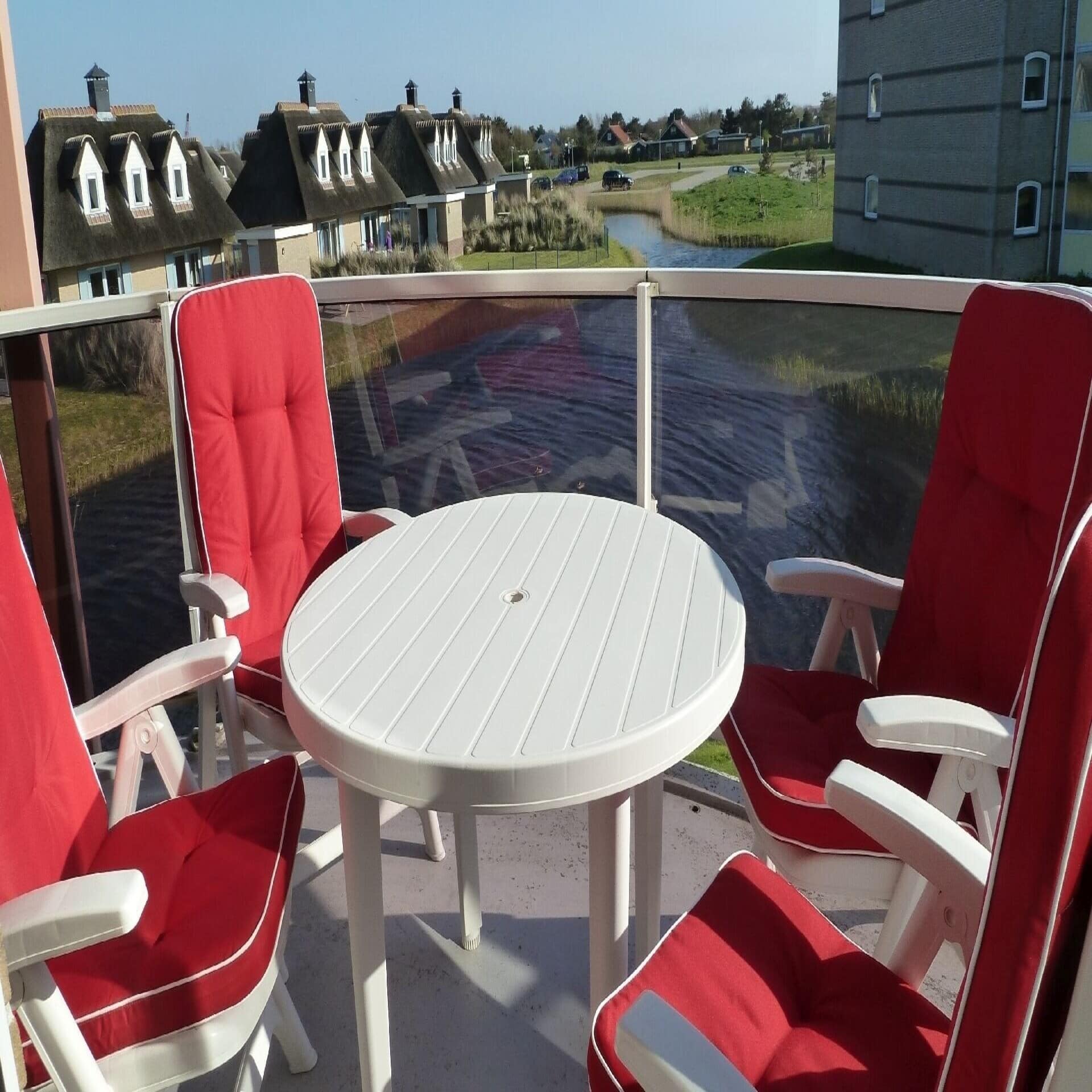 Blick vom Balkon mit Tisch und 4 Stühlen mit roten Polstern und Blick auf das Wasser und Häuser. 