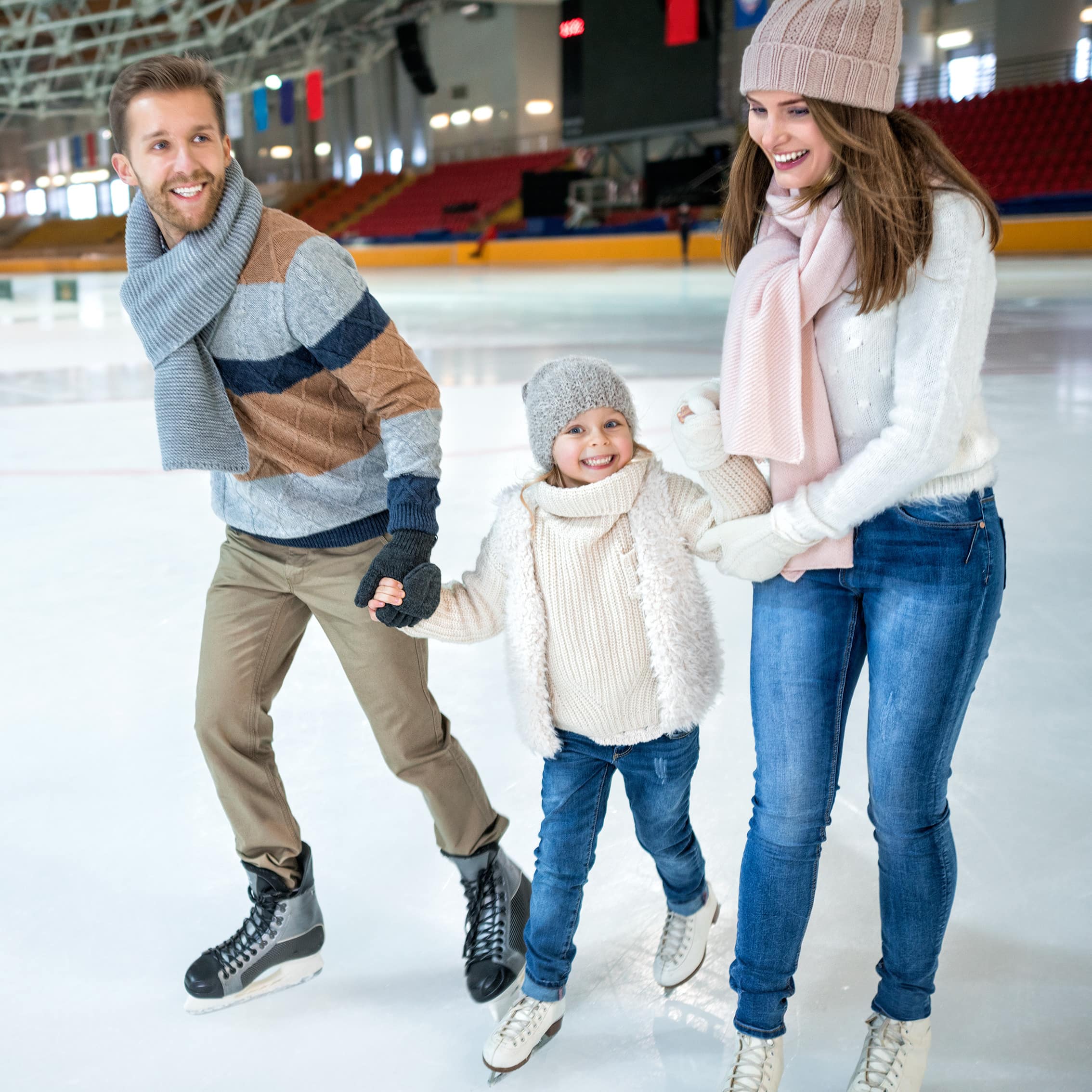 Vater und Mutter mit Tochter an der Hand beim Schlittschuhlaufen in der Eishalle.