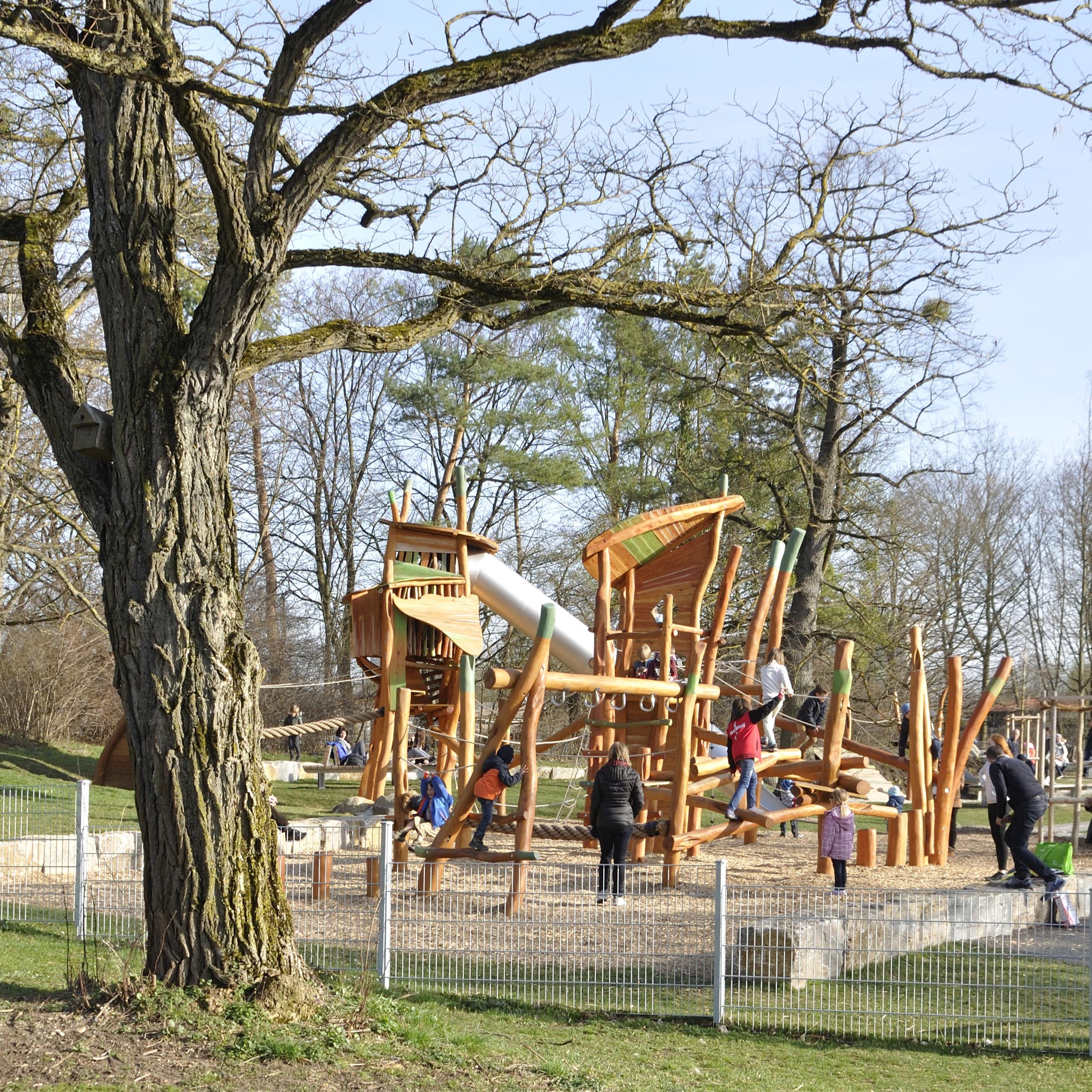 Blick auf einen Spielplatz mit großem Holzklettergerüst in einem Park im München.