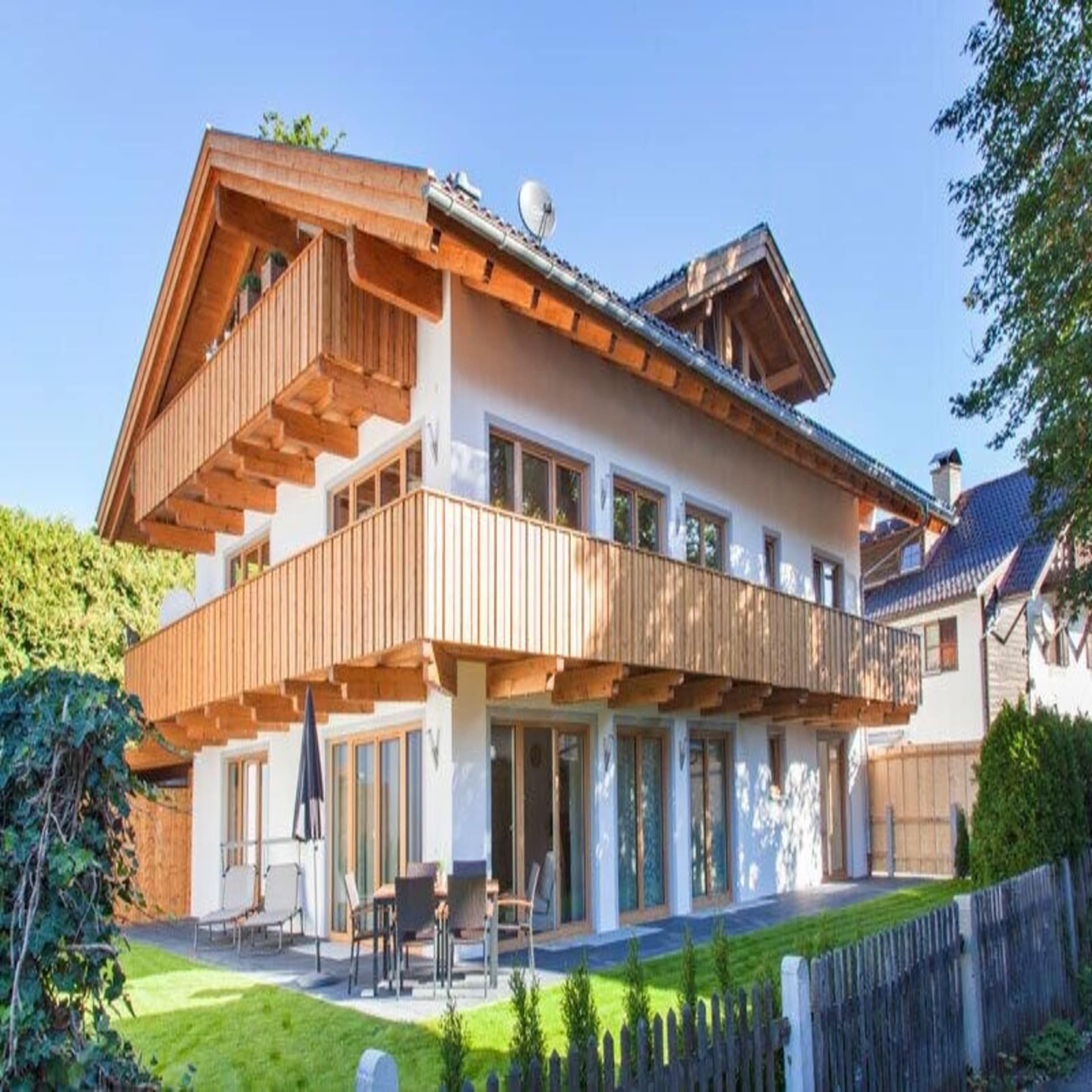 Blick auf ein modernes, bayerisches Haus mit heller Holzverkleidung und Garten.