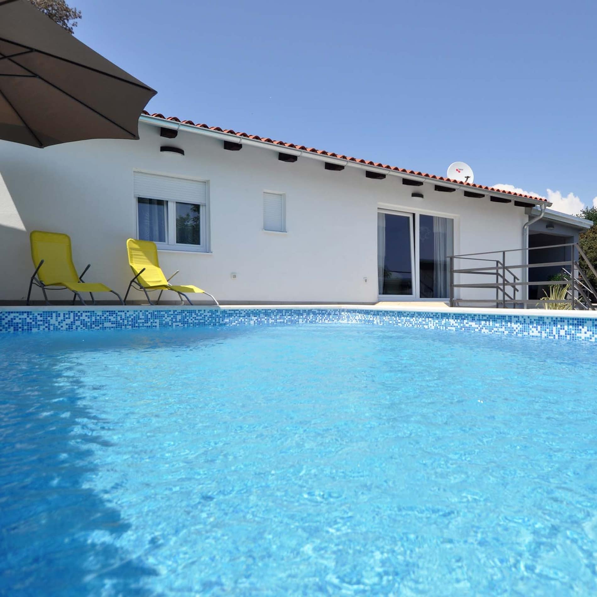 Großzügiges Ferienhaus in Pula mit blauem Pool im Vordergrund und zwei Liegestühlen