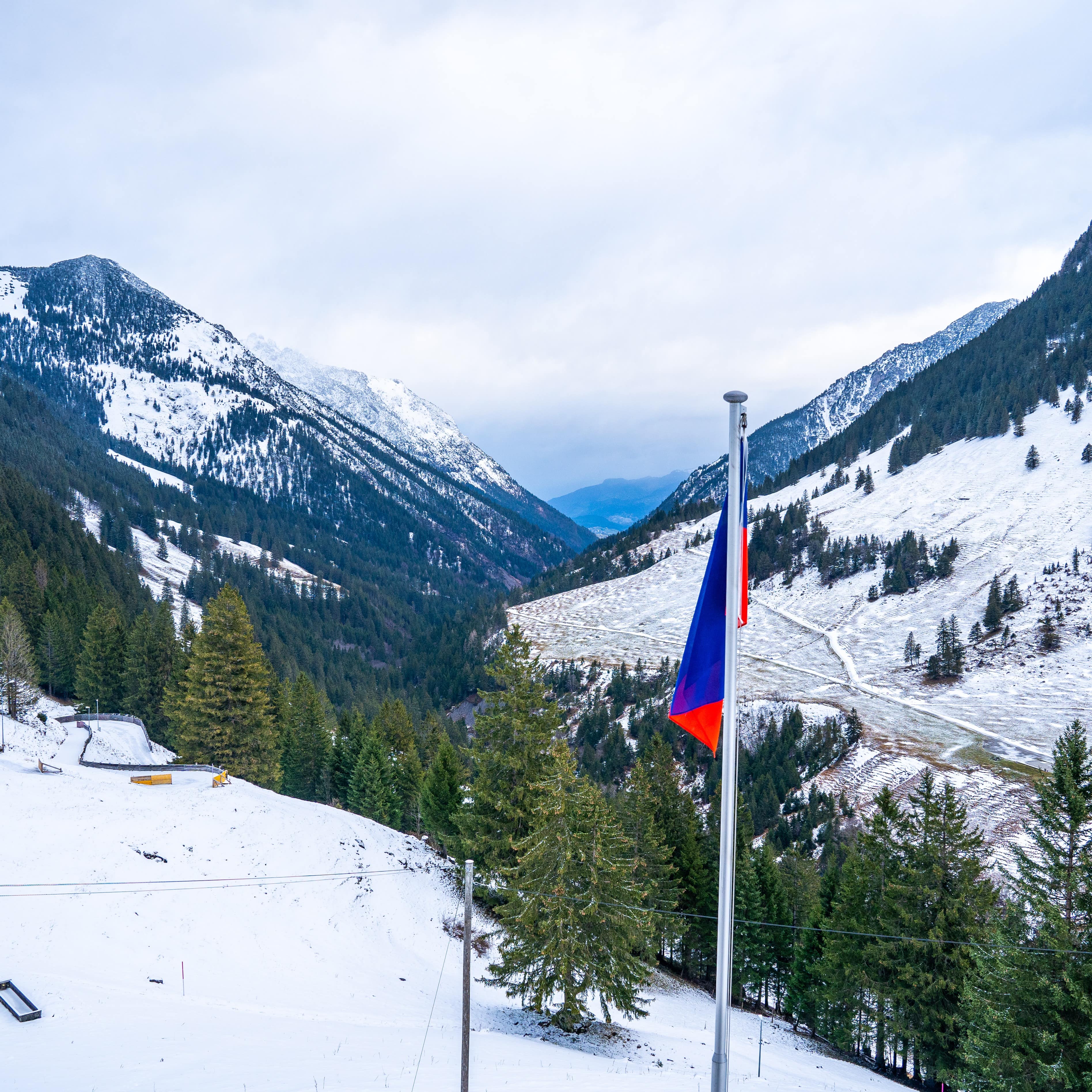 Blick über das verschneite und bewaldete Skigebiet Malbun, die Liechtensteiner Flagge im Vordergrund.