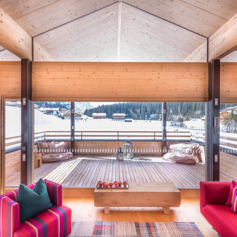 Ferienhaus in Vorarlberg mit großem Wohnraum und Fensterfront, Terrasse und Blick über ein verschneites Dorf und die Berge