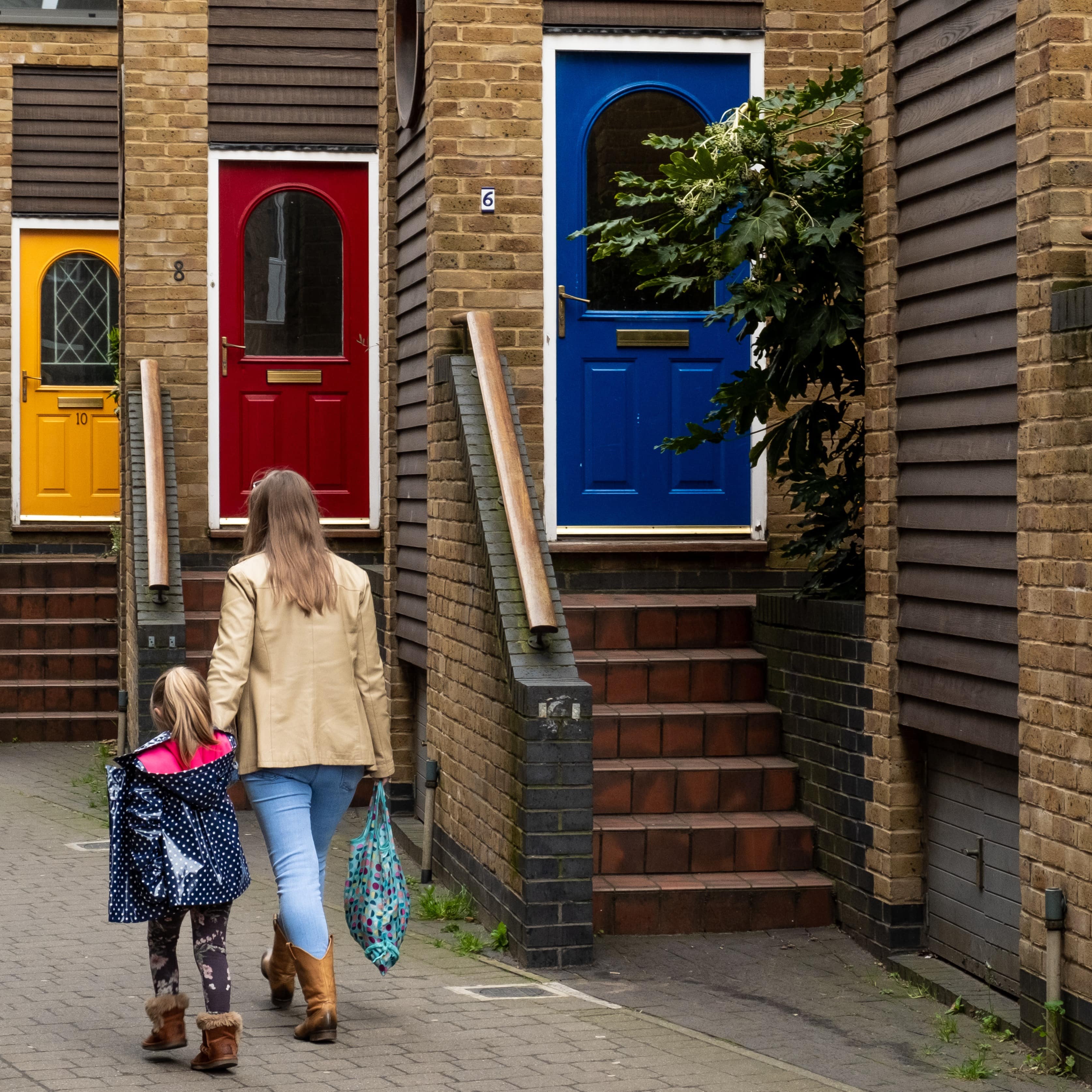 Rückenansicht: Mutter und Tochter laufen bräunlichen Häusern mit bunten 