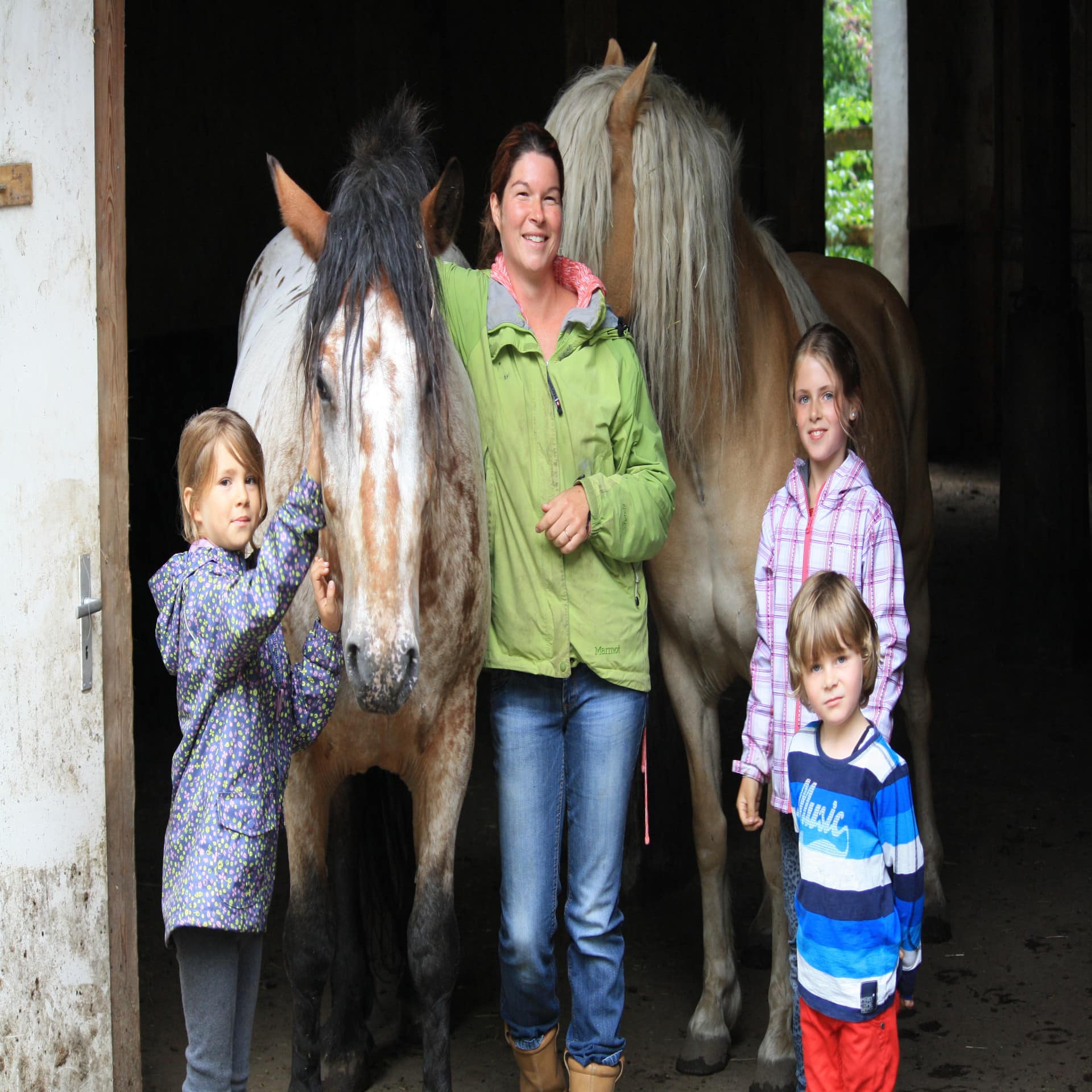 3 Kinder und 1 Frau mit 2 Ponys im Stall. 