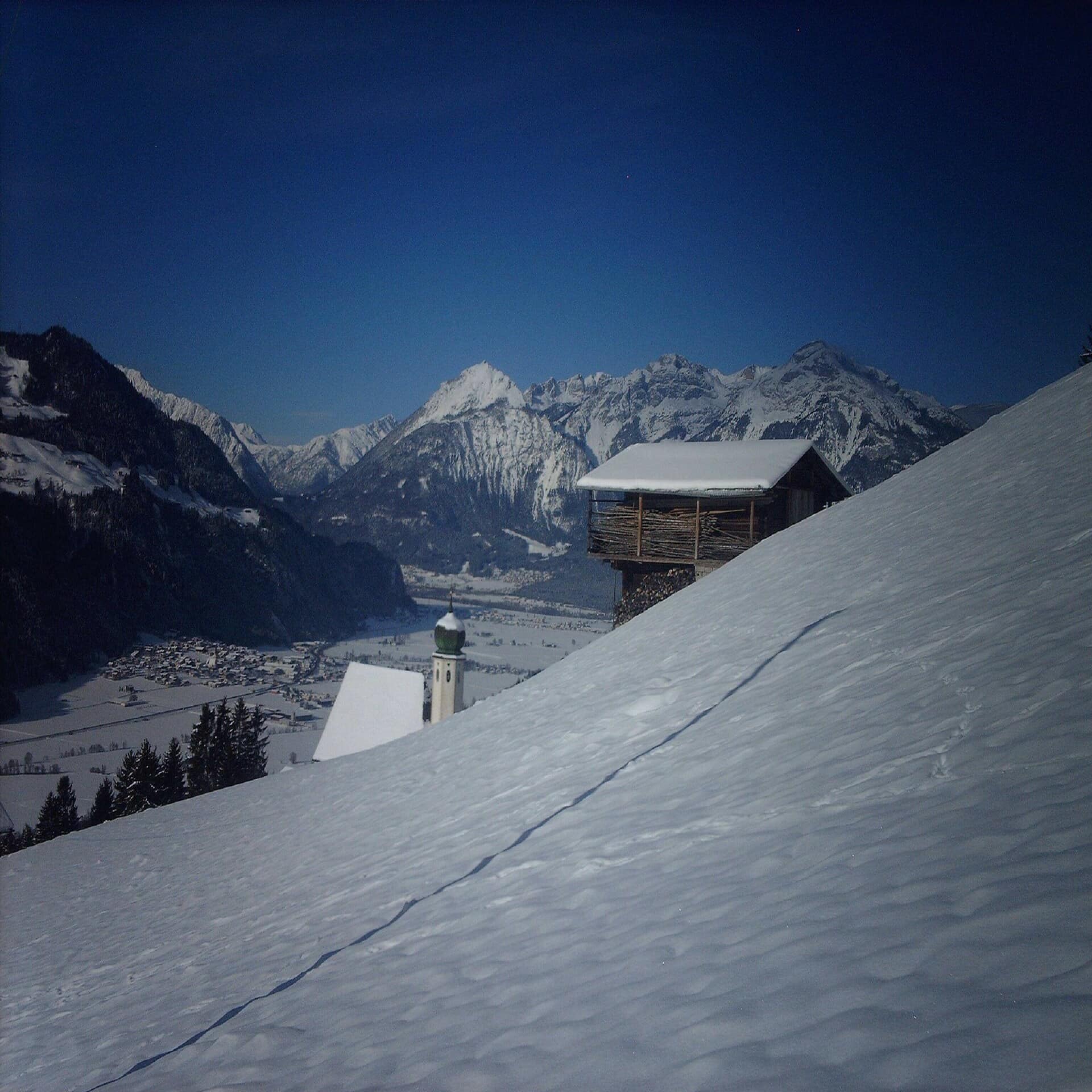 Blick von einem Berg auf eine kleine Hütte und das Zillertal. Es ist Winter und überall liegt Schnee.