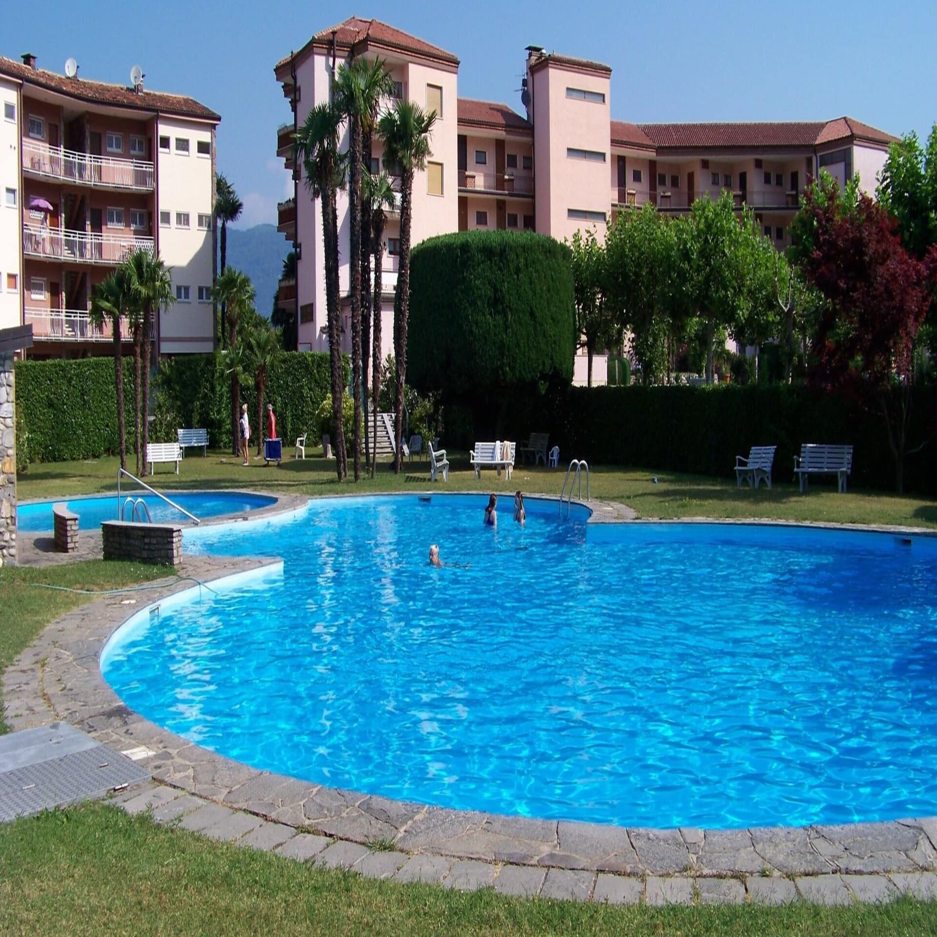 Personen schwimmen in einem Pool im Garten einer Apartmentanlage. 