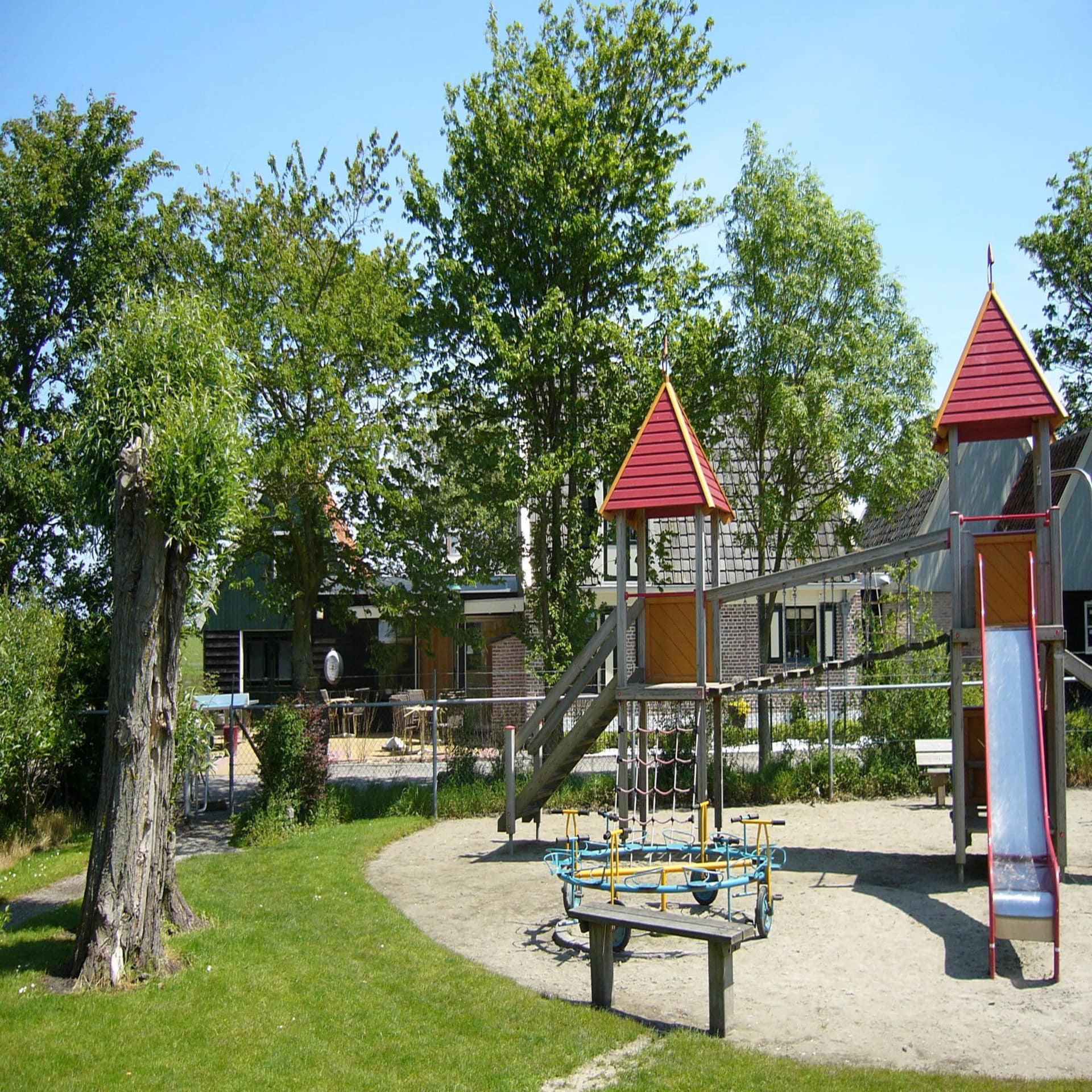 Spielplatz und ein Haus dahinter in einem Ferienpark. 