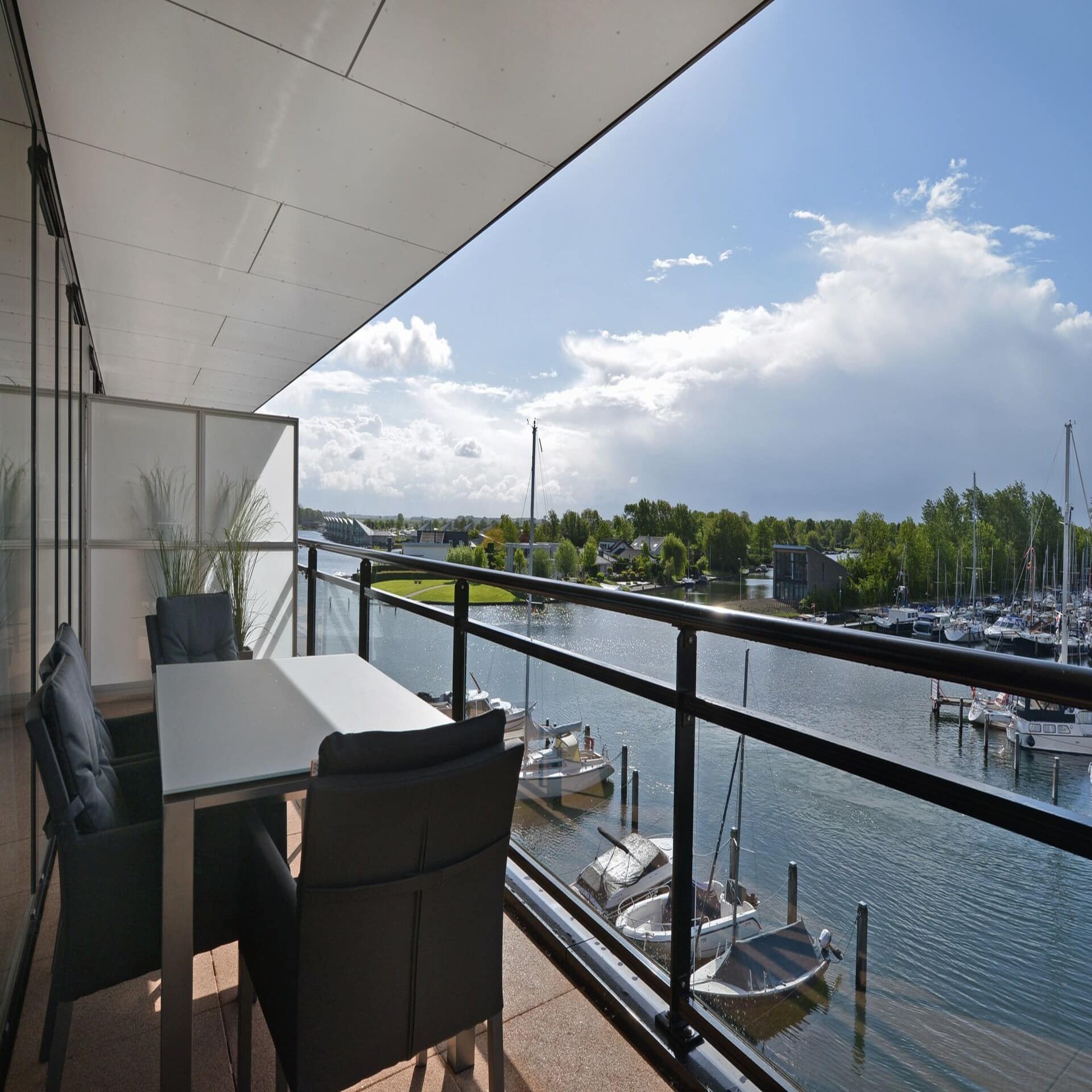 Balkon mit Tisch und Stühlen und Blick auf einen Jachthafen. Die Sonne scheint. 