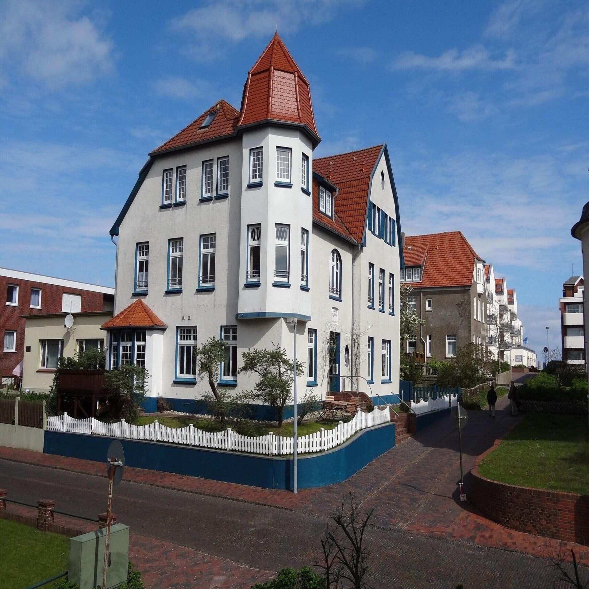 Weißes Haus mit rotem Dach und blauen Verzierungen in einem Ort auf Wangerooge.