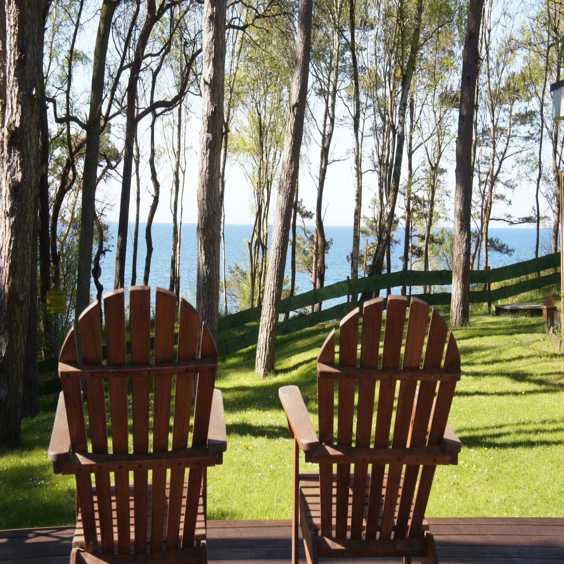  2 Stühle auf einer Holzveranda mit blick auf den grünen Garten und das Meer. 
