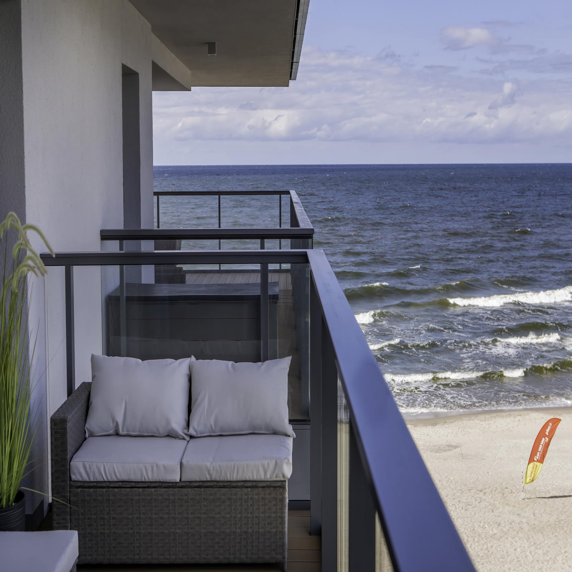 Balkon mit Glasfassade und kleinem Sofa direkt am Strand.