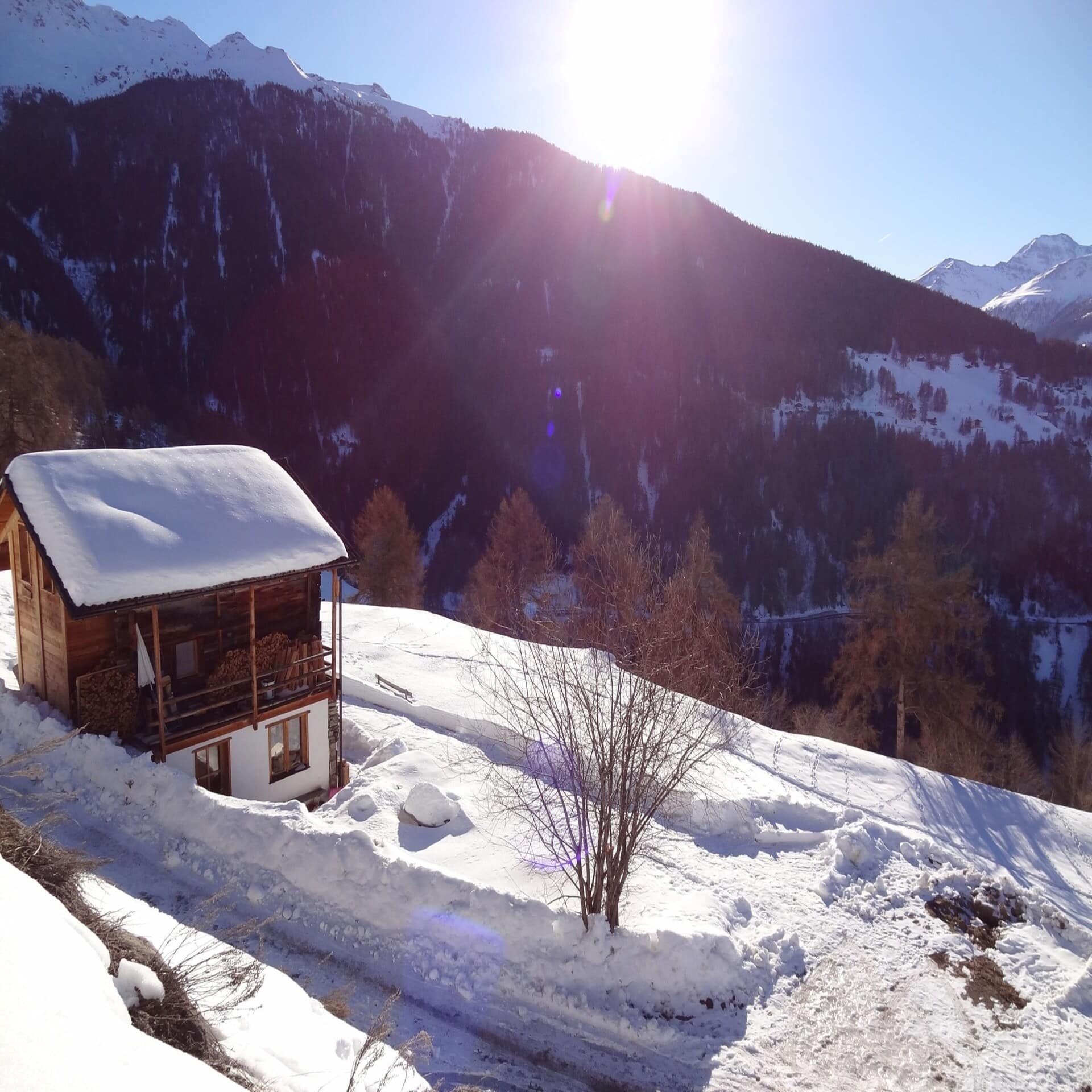 Kleines Chalet an einem verschneiten Berghang mit Panoramablick auf die Umgebung. Die Sonne scheint.