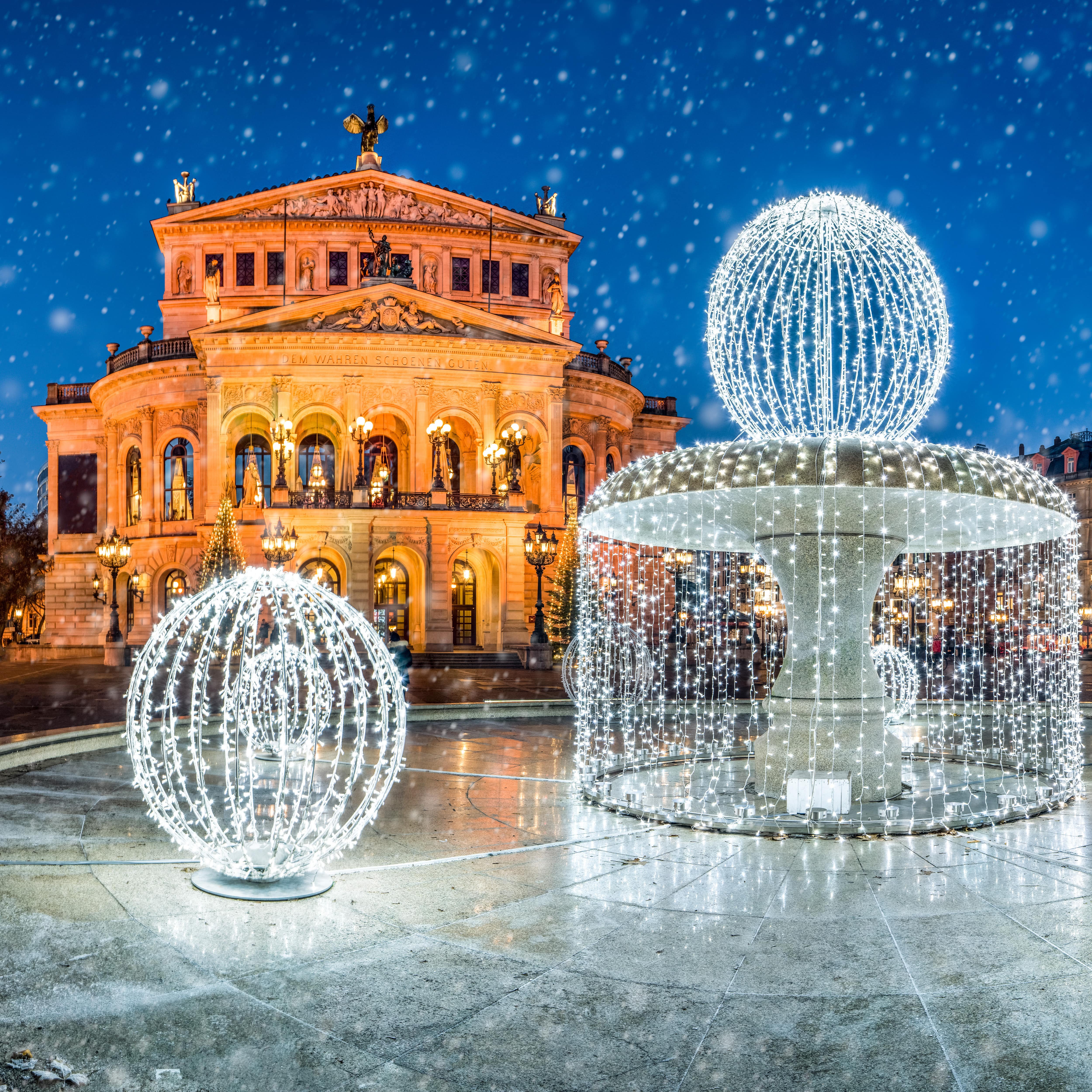 Blick auf den erleuchteten Brunnen und die Alte Oper bei Schneefall am Abend. 
