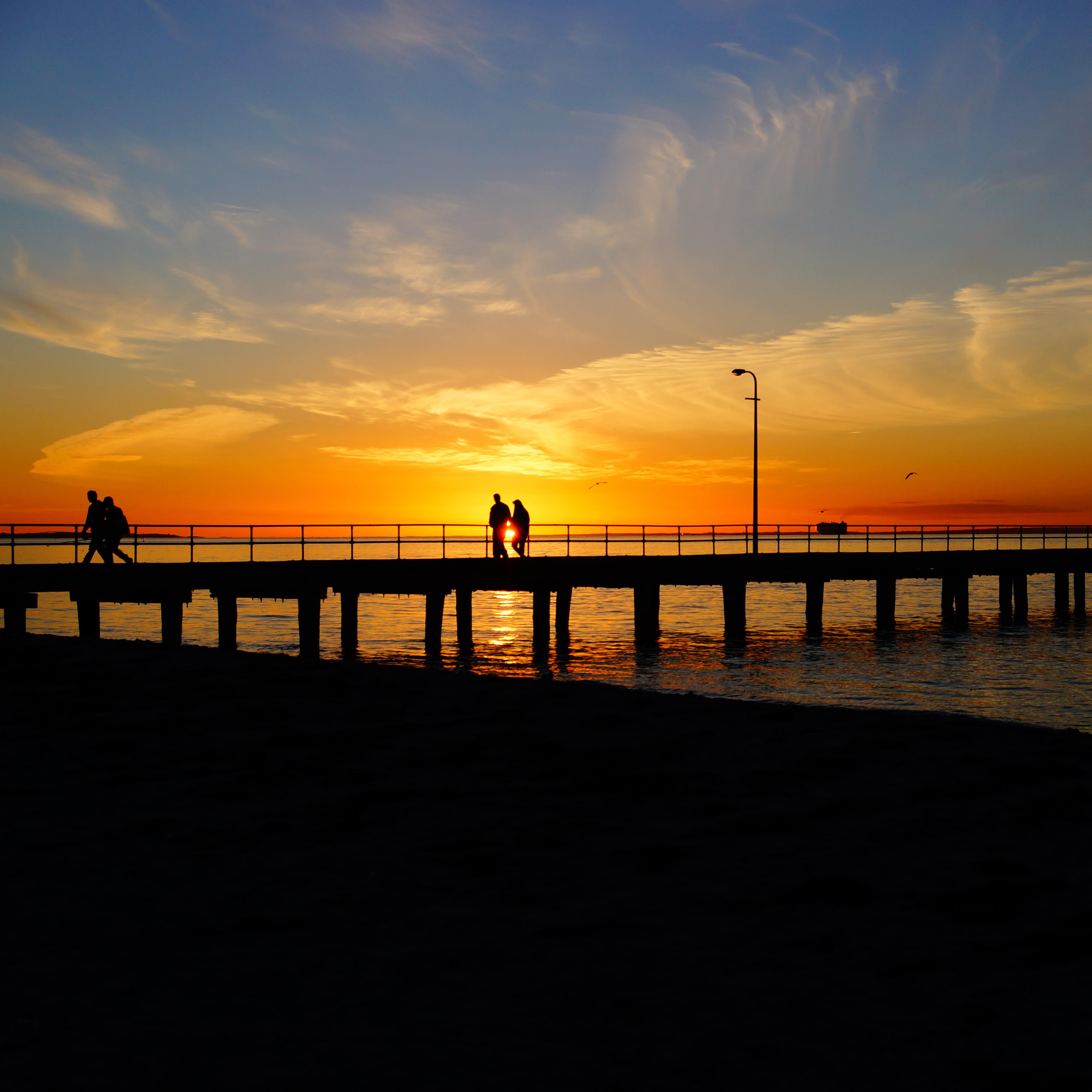 Golden sunset over an Australian beach and pier with shadows of couples walking