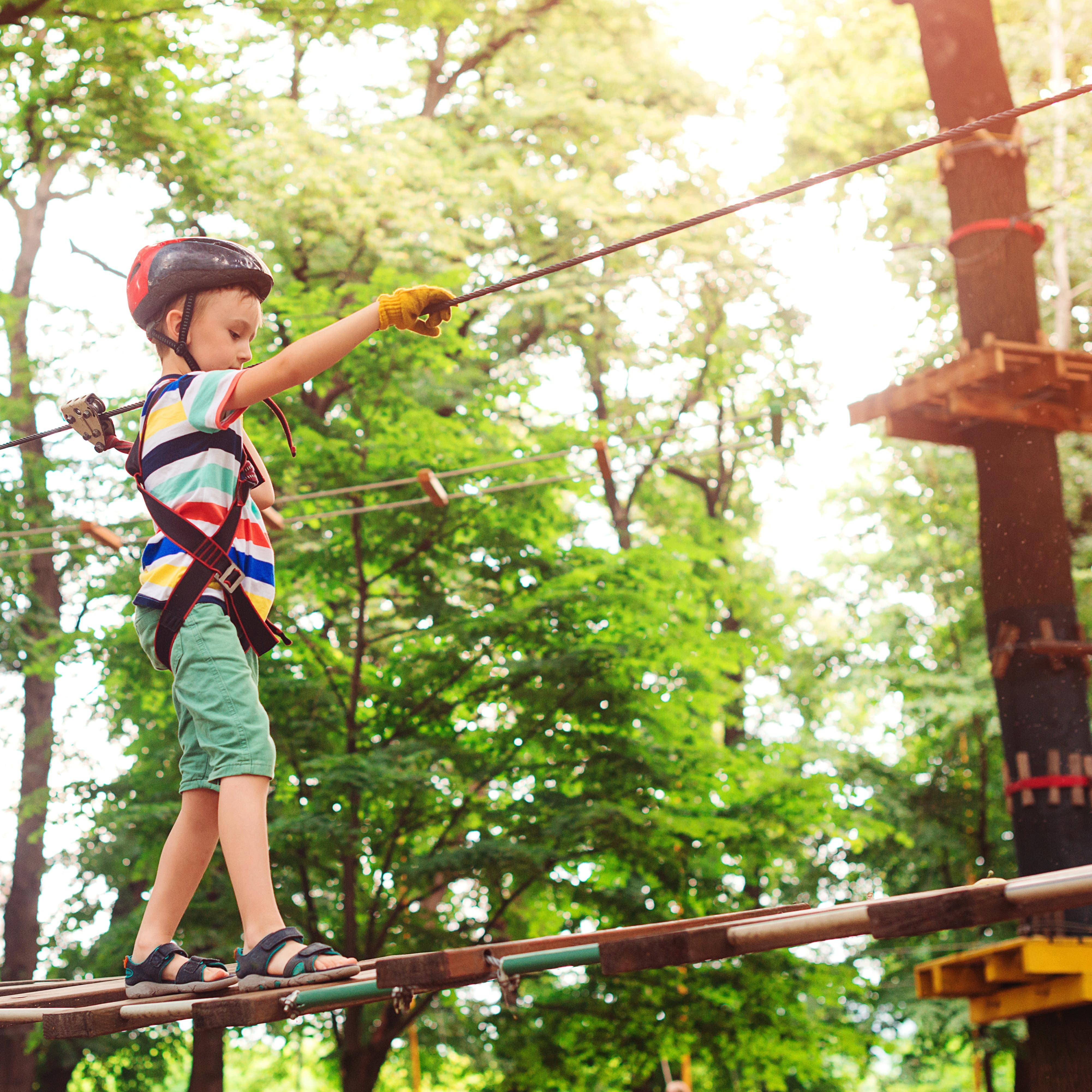 Junge mit Helm und Gurt balanciert auf einem schwankenden Holzpfad. 