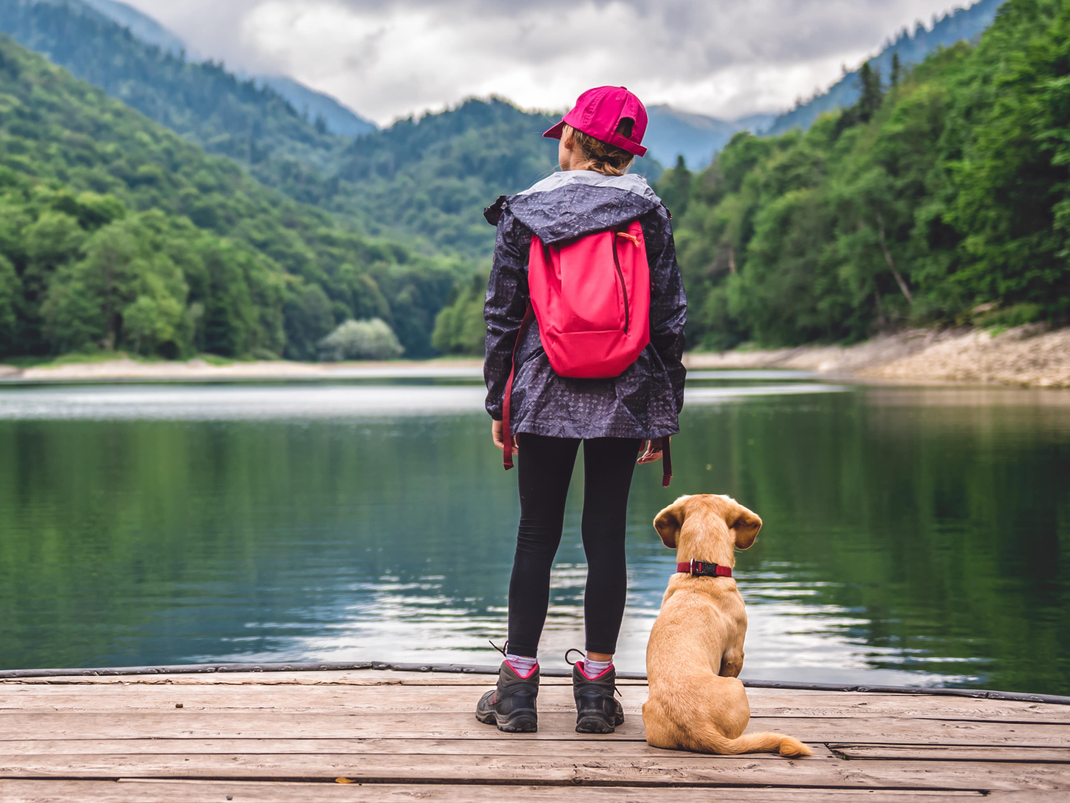 kleines Mädchen in Wanderkleidung auf einem Dock mit ihrem Hund