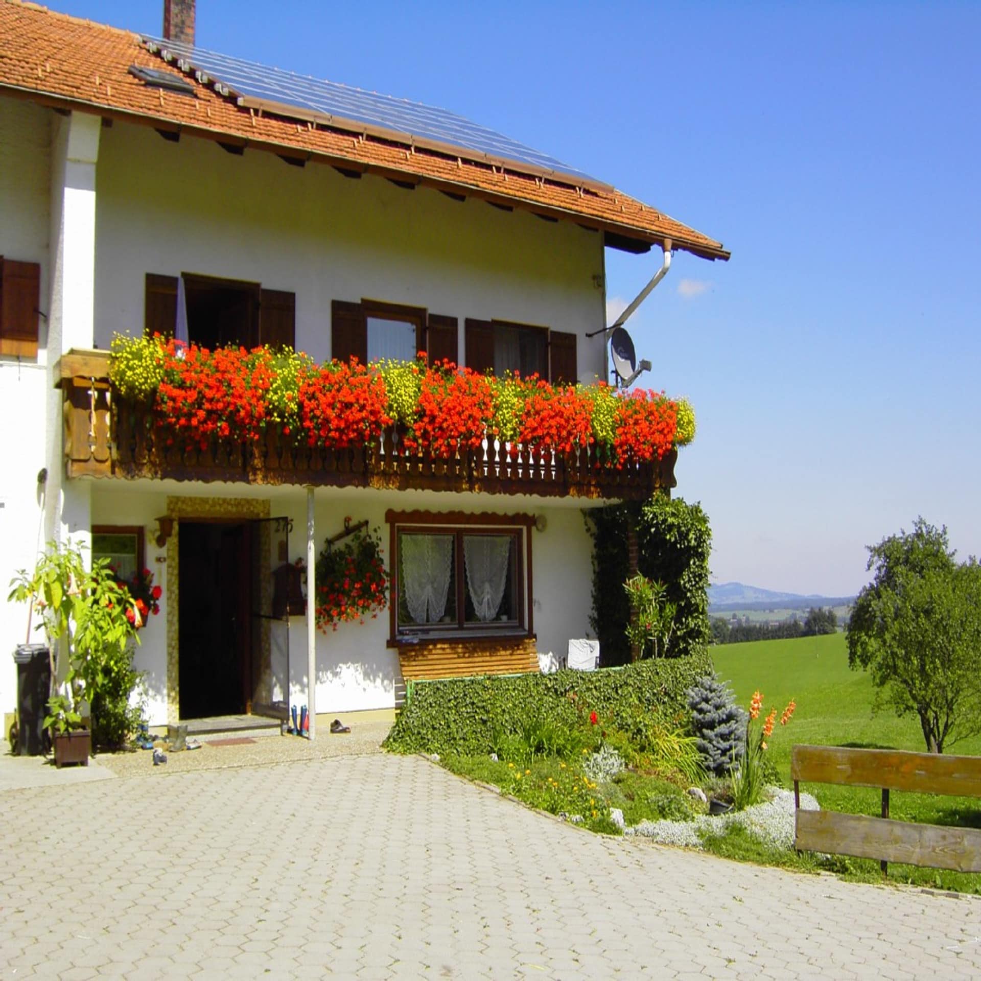 Bauernhaus mit roten Geranien am Balkon und Blick auf die grüne Umgebung im Allgäu. 