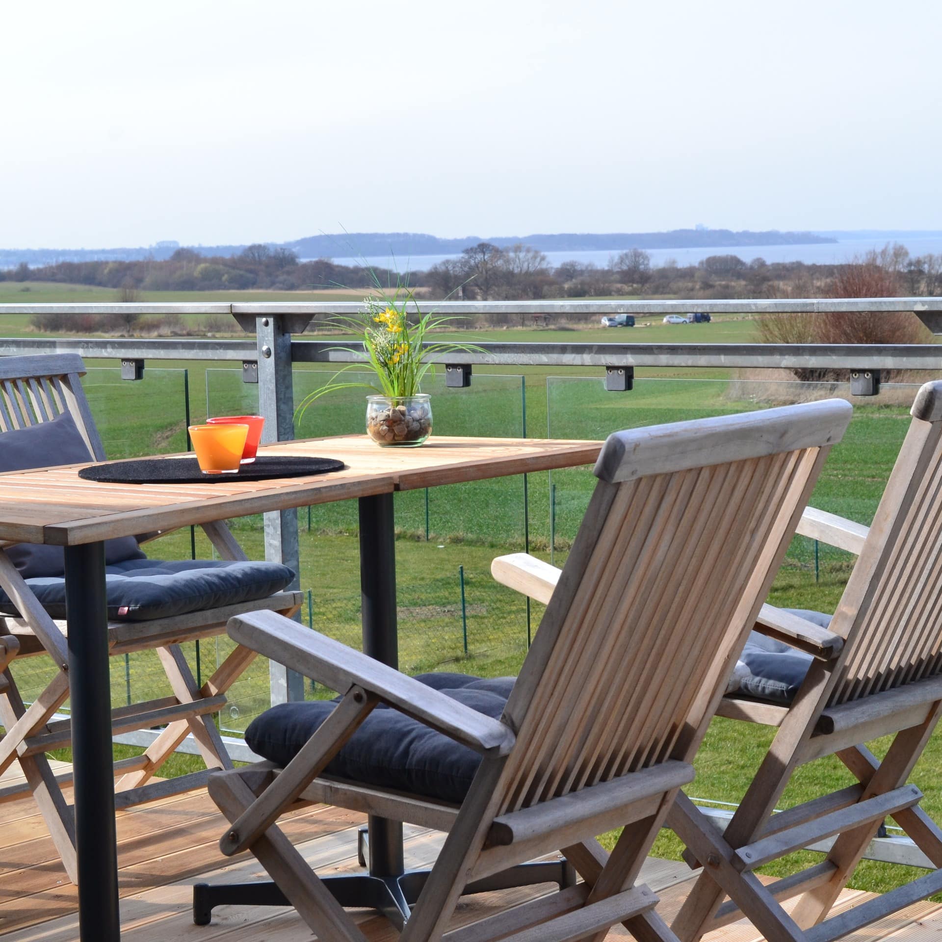 Balkon mit Glasfassade und Tisch mit vier Stühlen und Blick auf das Wasser in einer Ferienwohnung in Boltenhagen  