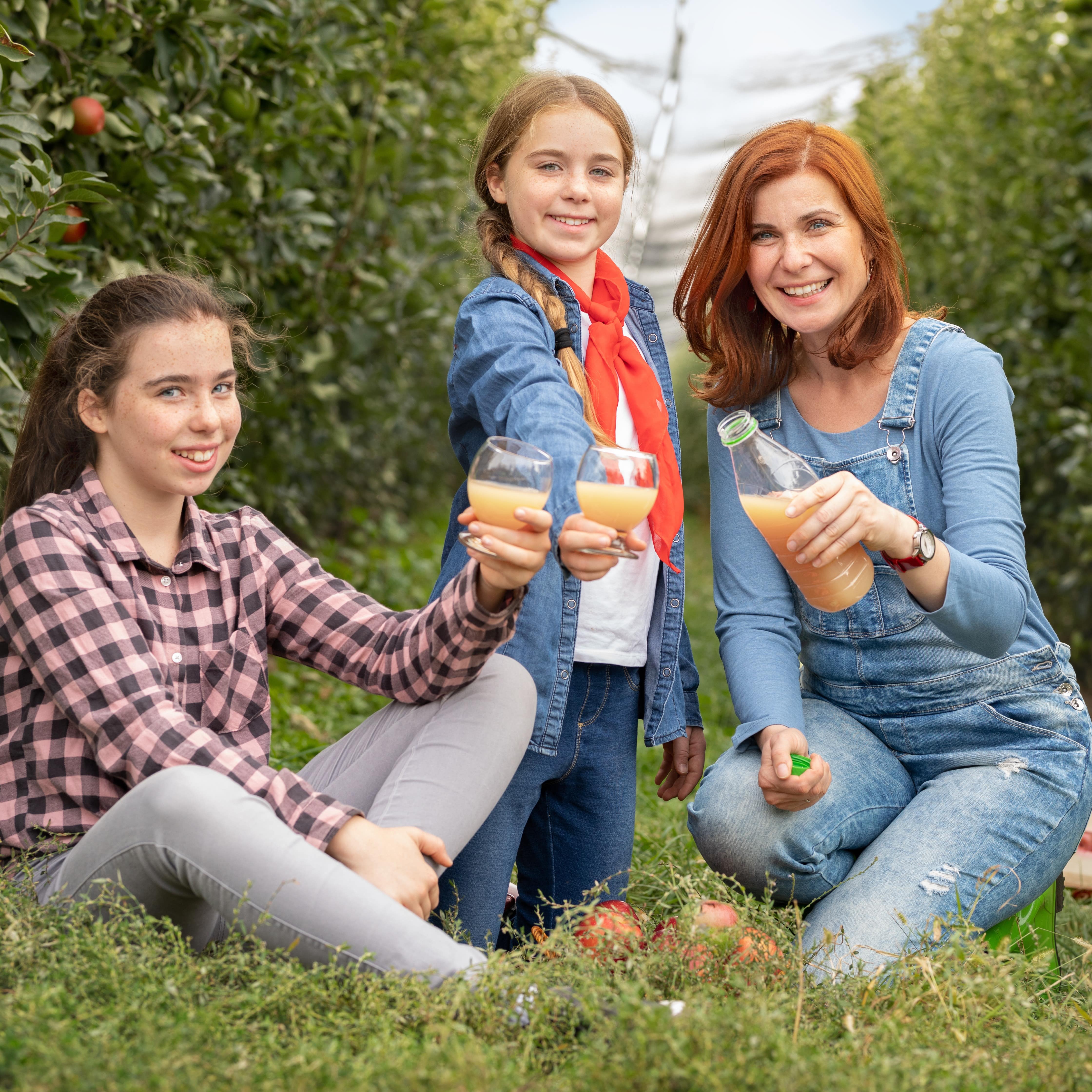 Eine Mutter und zwei Mädchen trinken Saft in einer Obstplantage