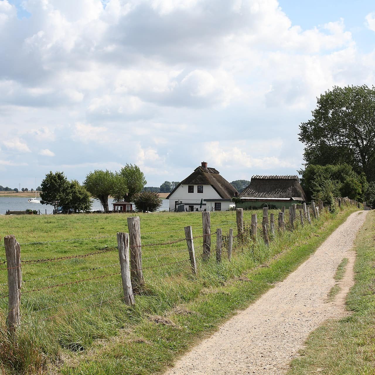 Ein Haus mit Reetdach direkt an der Schlei, umgeben von einer Wiese, daneben verläuft ein Spazierweg.