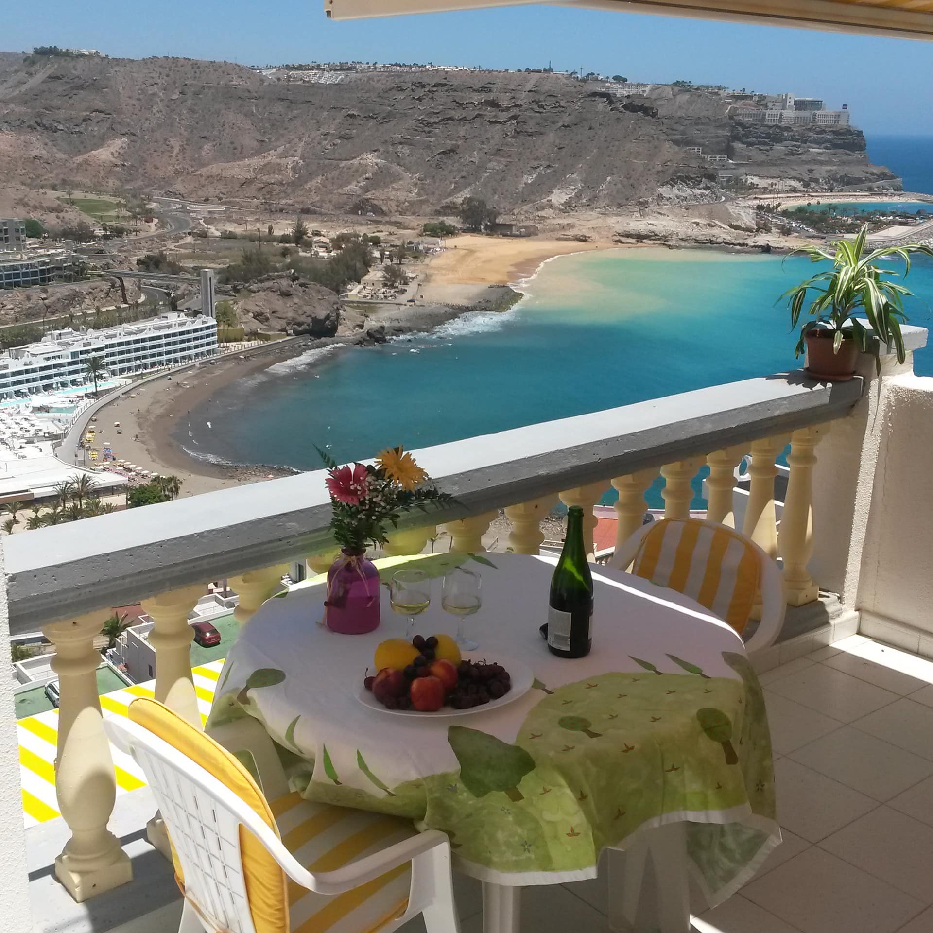 Ferienwohnung auf Gran Canaria mit Balkon, darauf ein gedeckter Tisch mit Stühlen, mit Blick über die Bucht und den Strand
