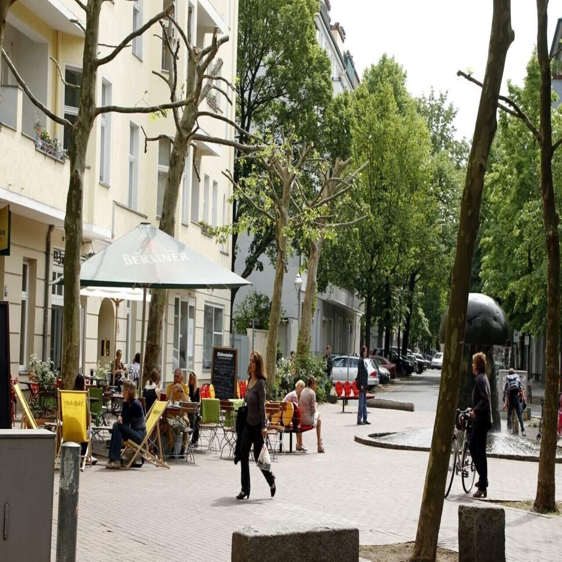 Restaurant auf einem Platz in einem Wohngebiet in Berlin. Eine Frau mit Einkaufstüten läuft vorbei.