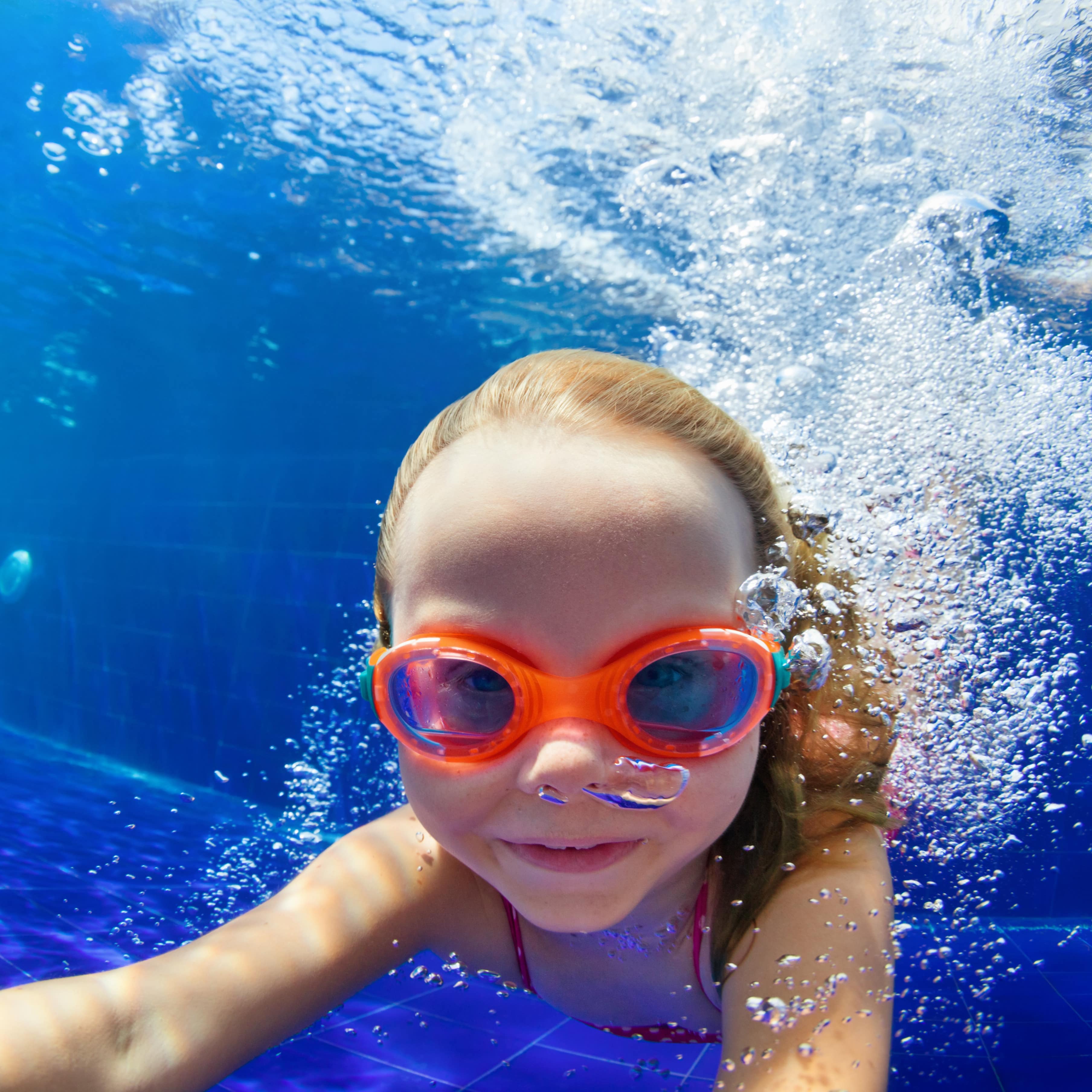 Ein Mädchen mit Schwimmbrille unter Wasser in einem Schwimmbecken.
