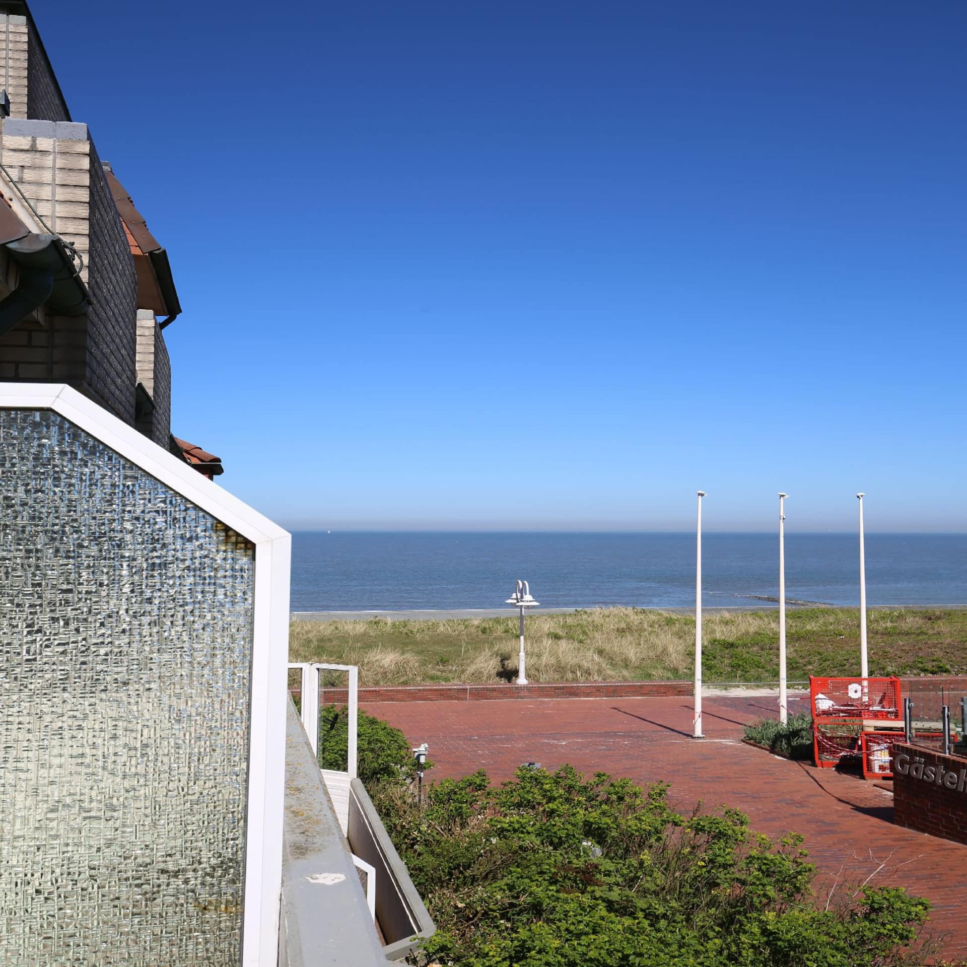 Blick vom Balkon einer Wohnung auf Wangerooge auf die Dünen und das Meer bei Sonnenschein.