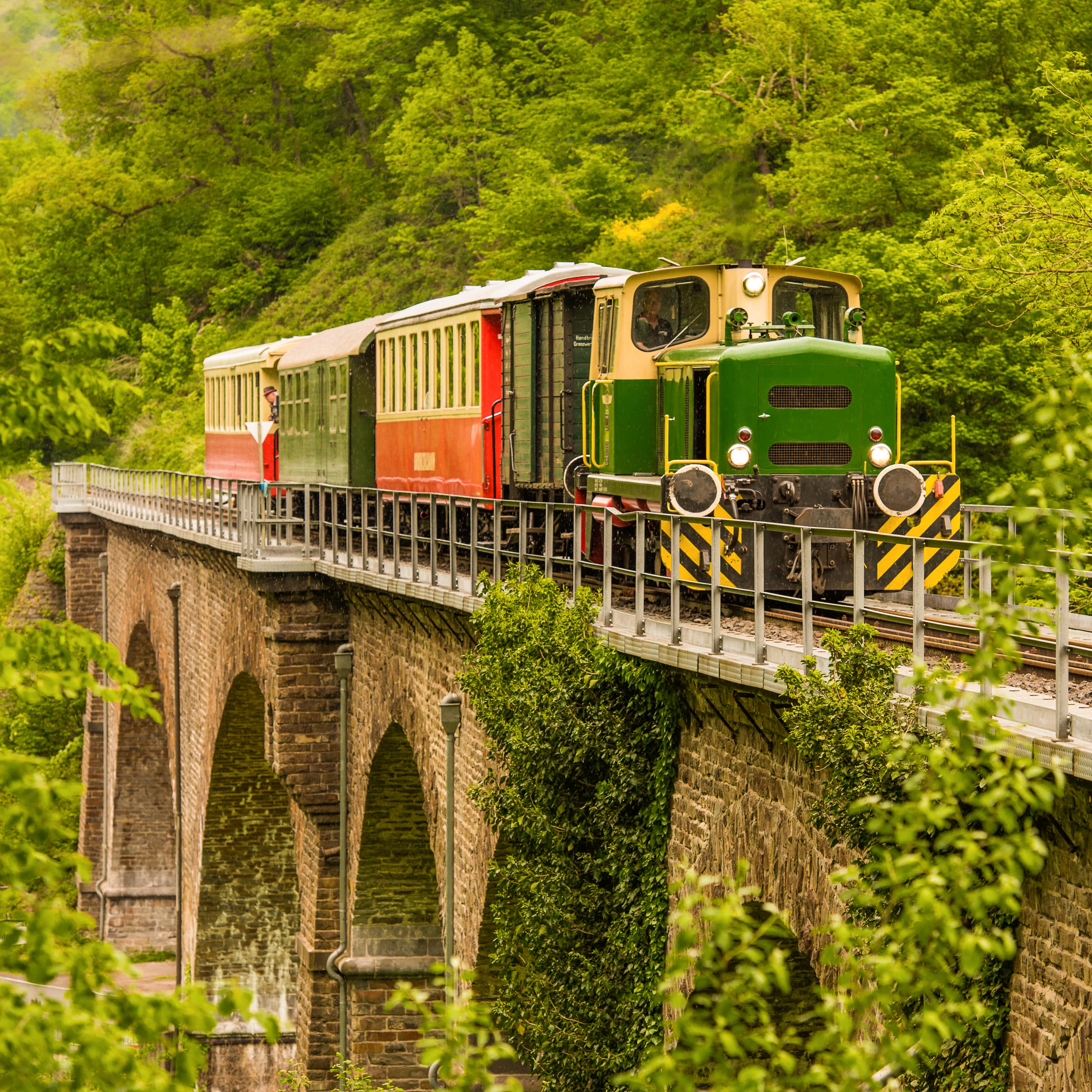 Der rot-gelb-grüne Vulkan-Express fährt über eine Viadukt Brücke.