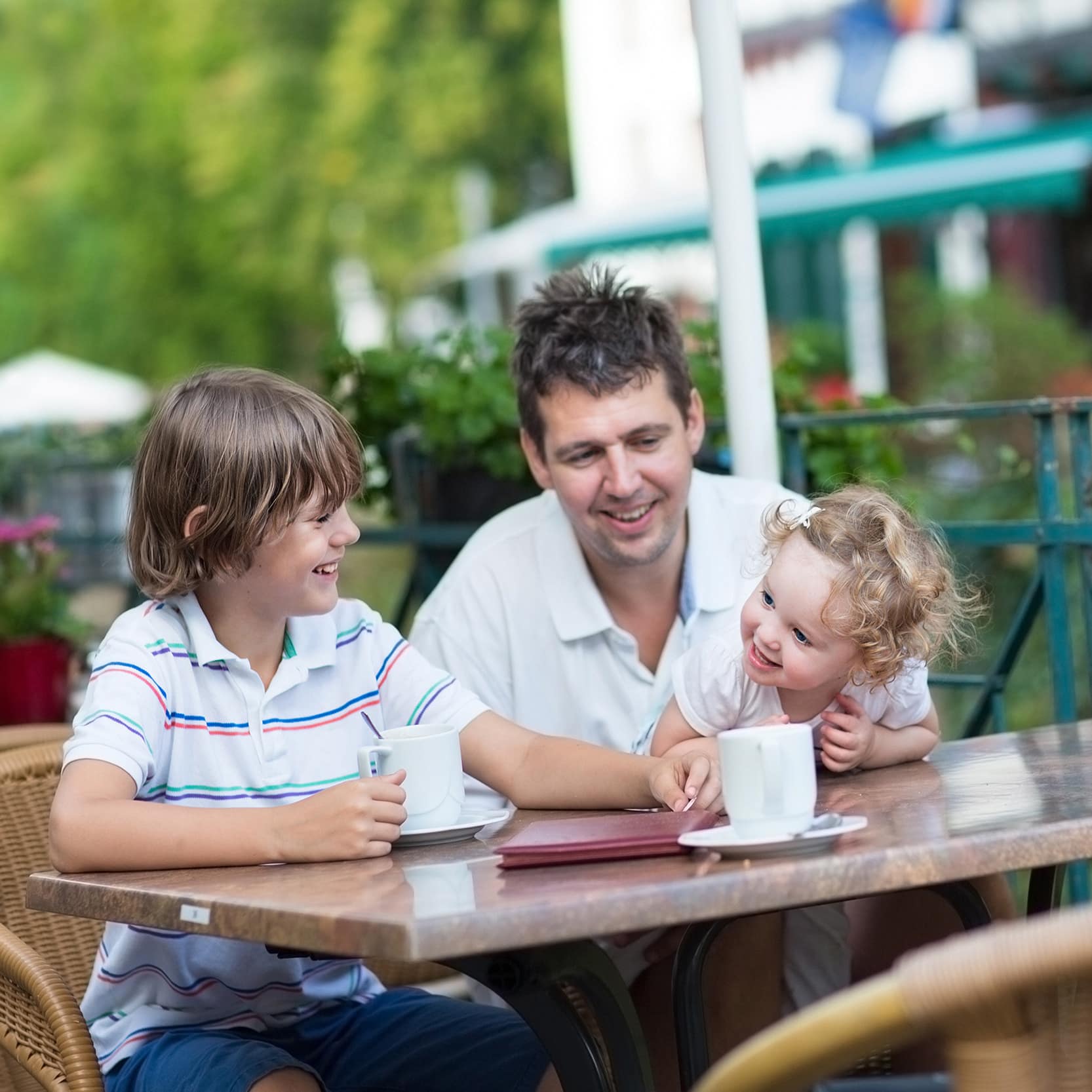 Vater, Sohn und Kleinkind an einem Gartentisch in einem Restaurant. Rechts steht ein Glas Bier.