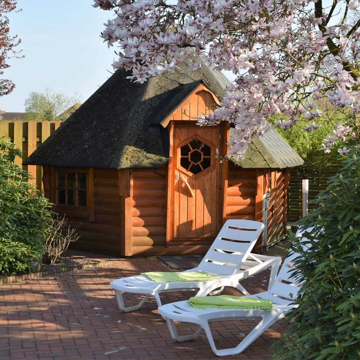 Blick auf eine Holzsauna im Garten mit 2 Liegestühlen davor