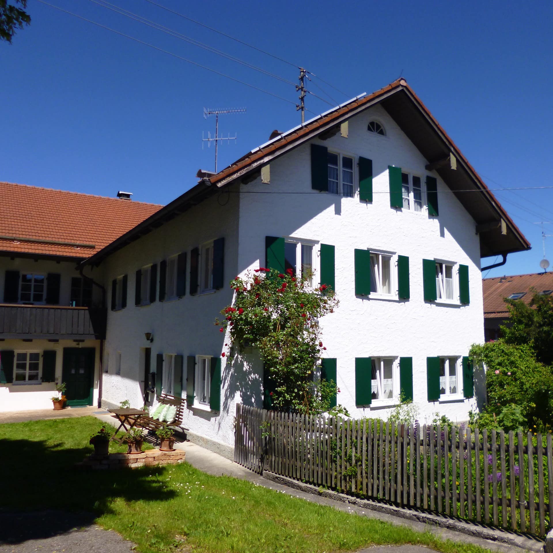 Ein weißes Bauernhaus mit grünen Fensterläden und Garten