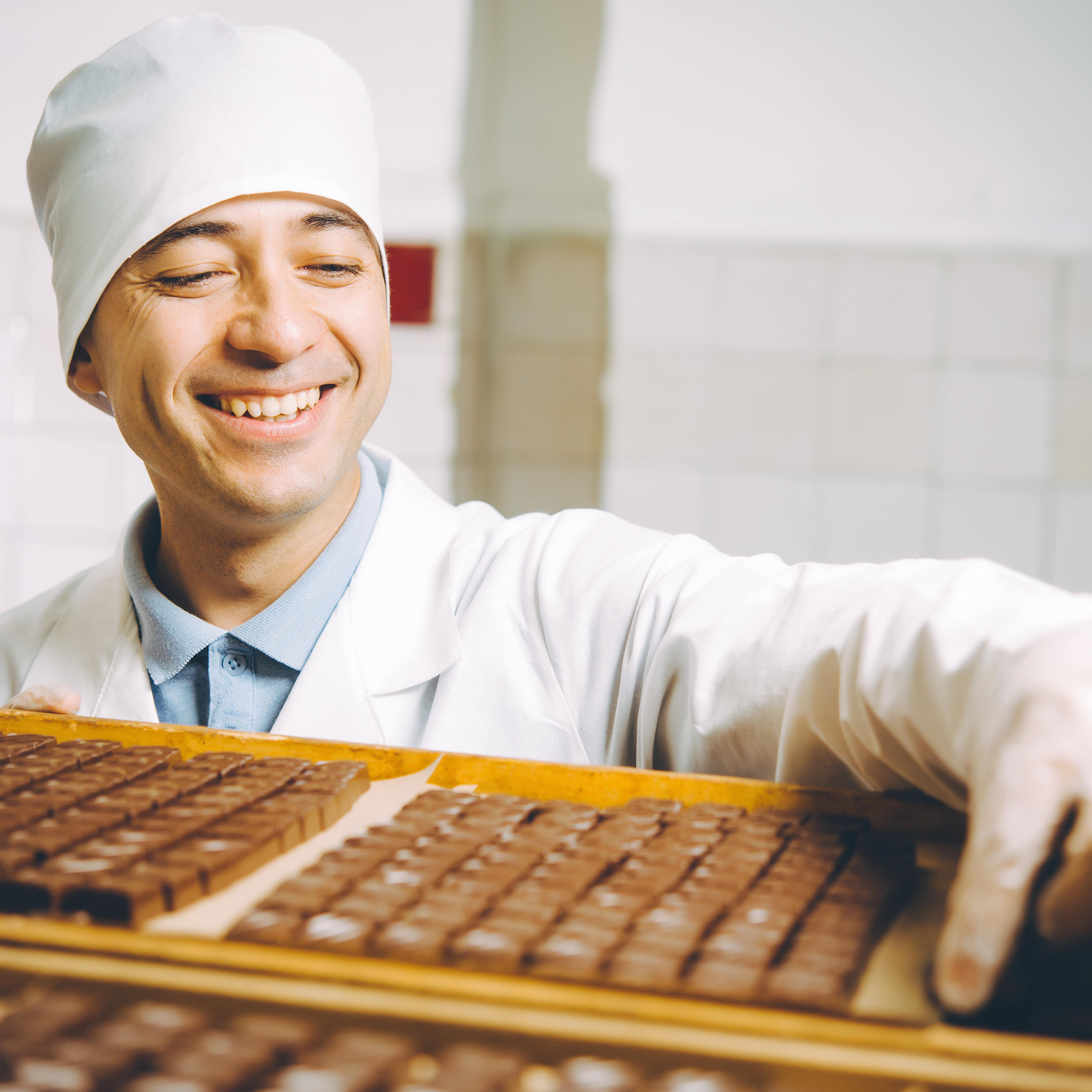 Ein lachender Mann in weißer Laborkleidung hantiert mit Pralinen.