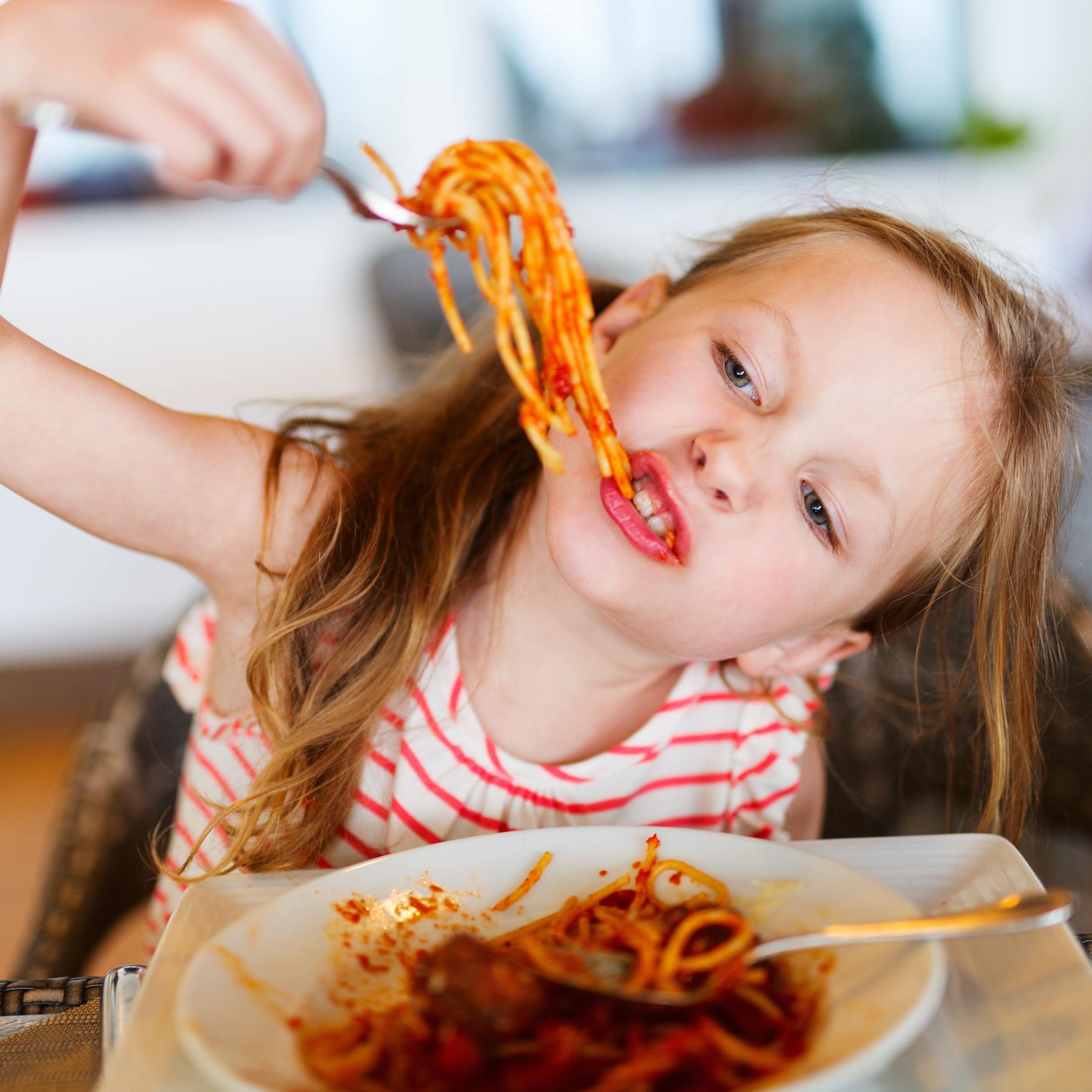 Nahaufnahme: Ein Mädchen in rot-weiß gestreiften T-Shirt isst Spaghetti mit Tomatensauce in einem Restaurant.