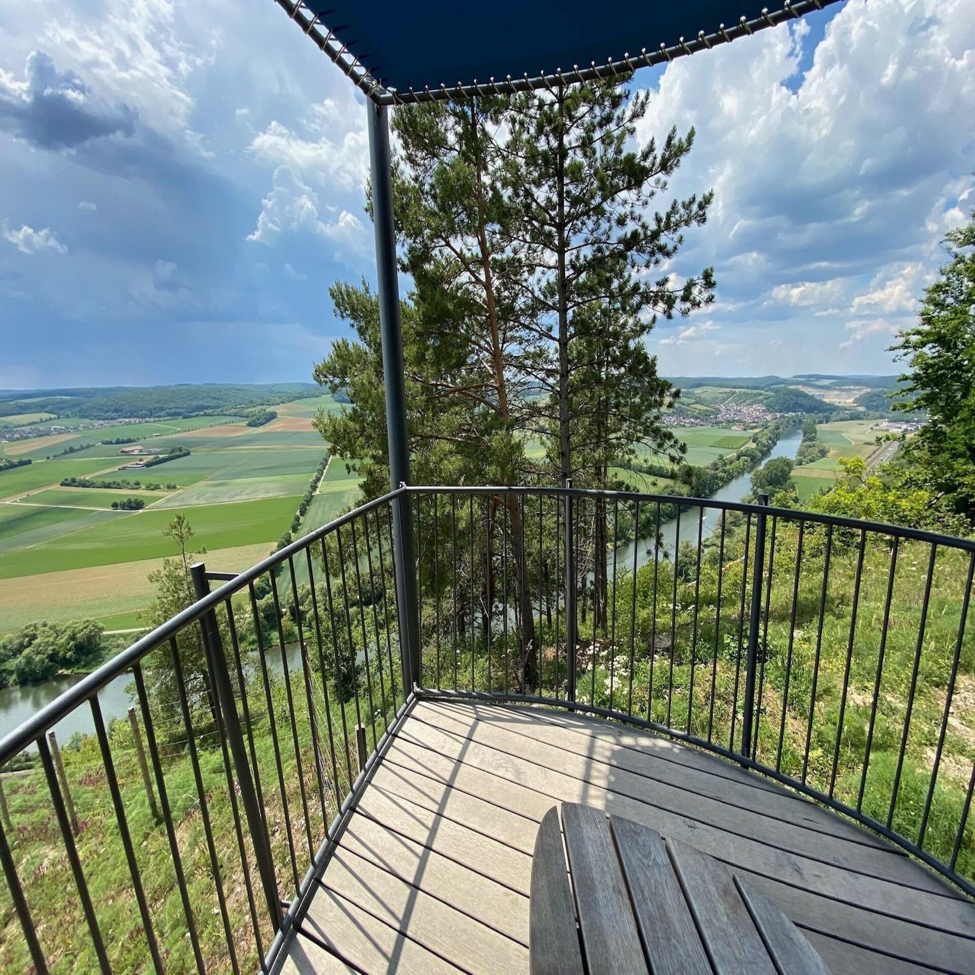 Blick vom Balkon auf einen Fluss und die ländliche Umgebung. Die Sonne scheint, Wolken am Himmel.