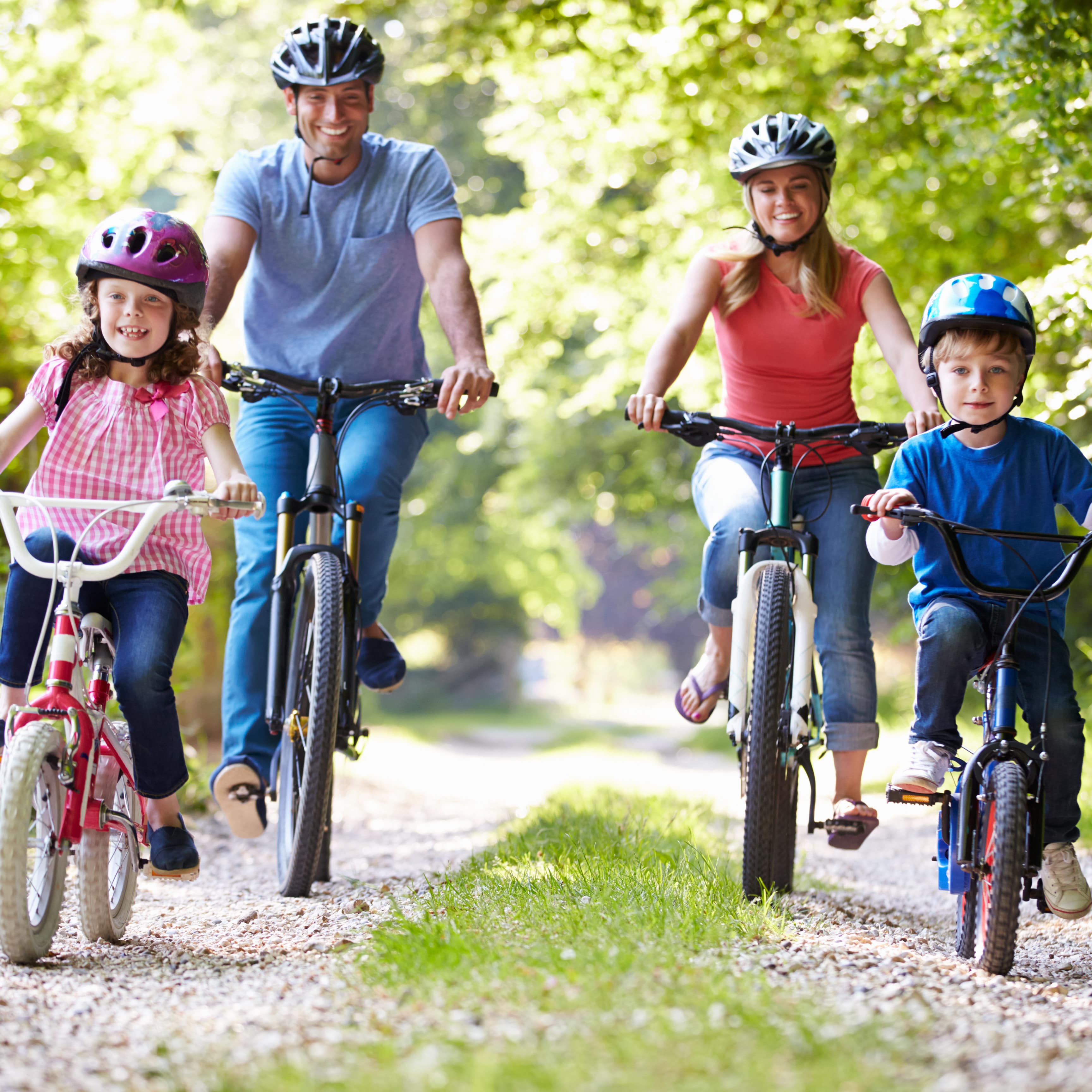 Eine Familie mit 2 Kindern machen eine Fahrradtour in ländlicher Umgebung, alle tragen Helme.