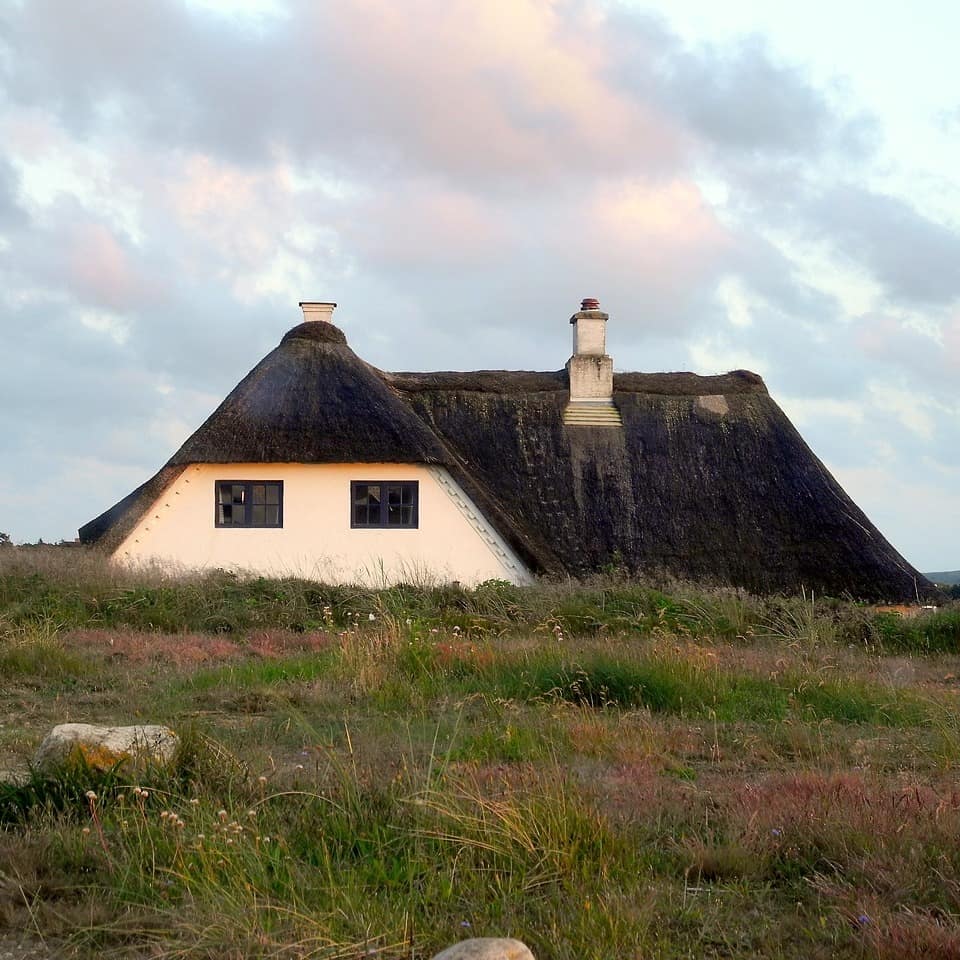 Ein Haus mit Reetdach liegt halb versteckt hinter einer grün bewachsenen Düne 