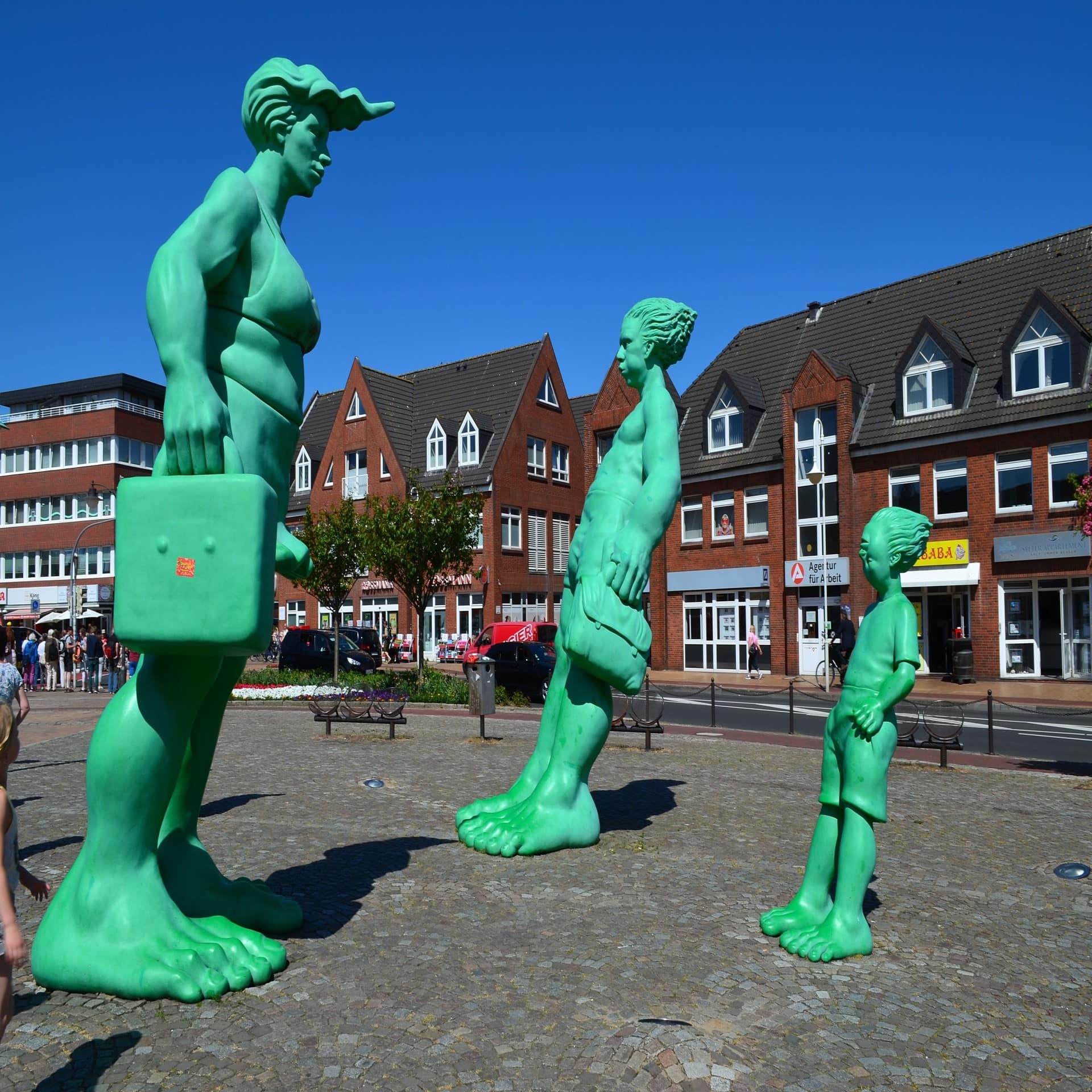 3 grüne Sturmfiguren vor den roten Häusern der Innenstadt von Westerland