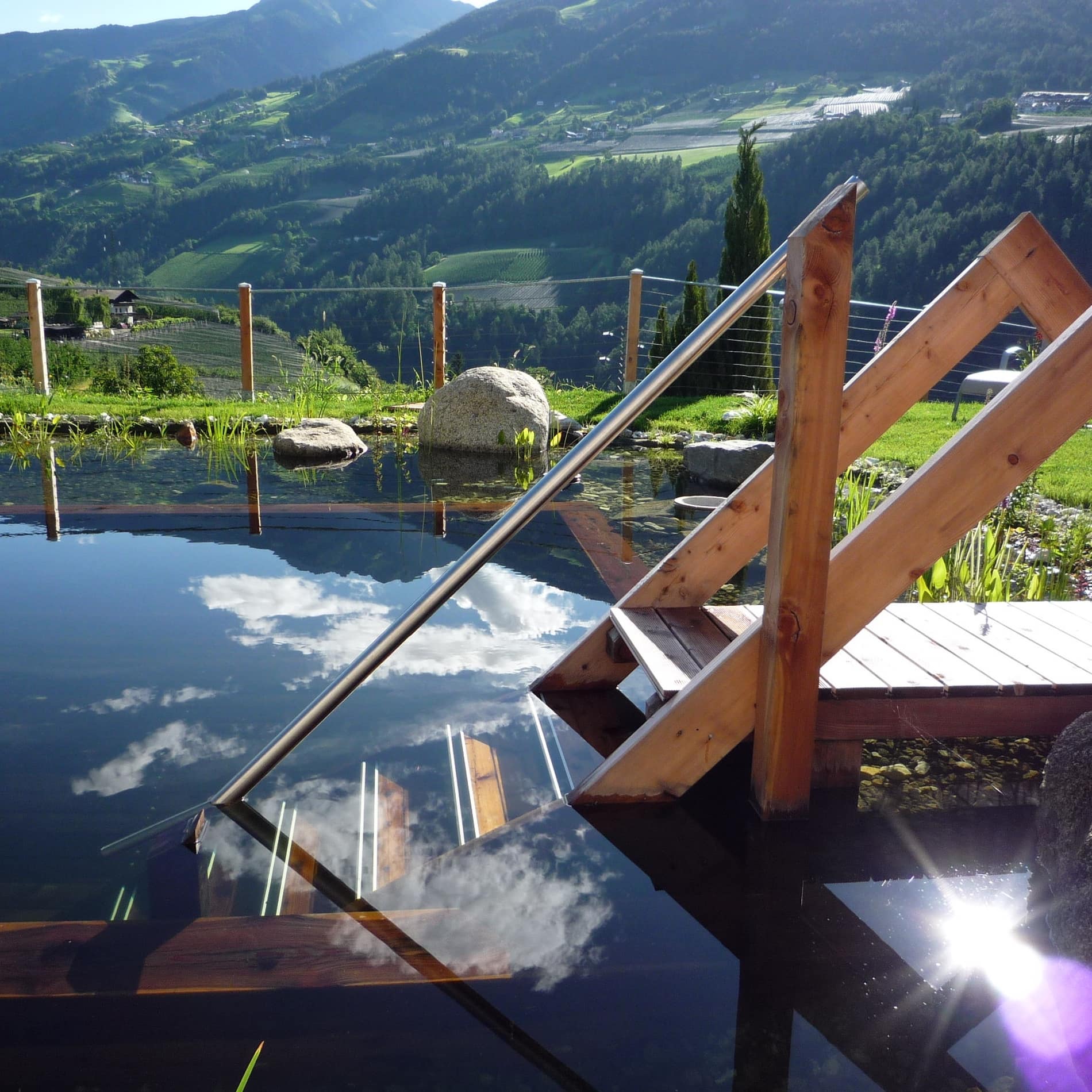 Eine Holztreppe führt ins Becken des Naturbadeteichs, der zur Ferienwohnung im Dorf Tirol gehört