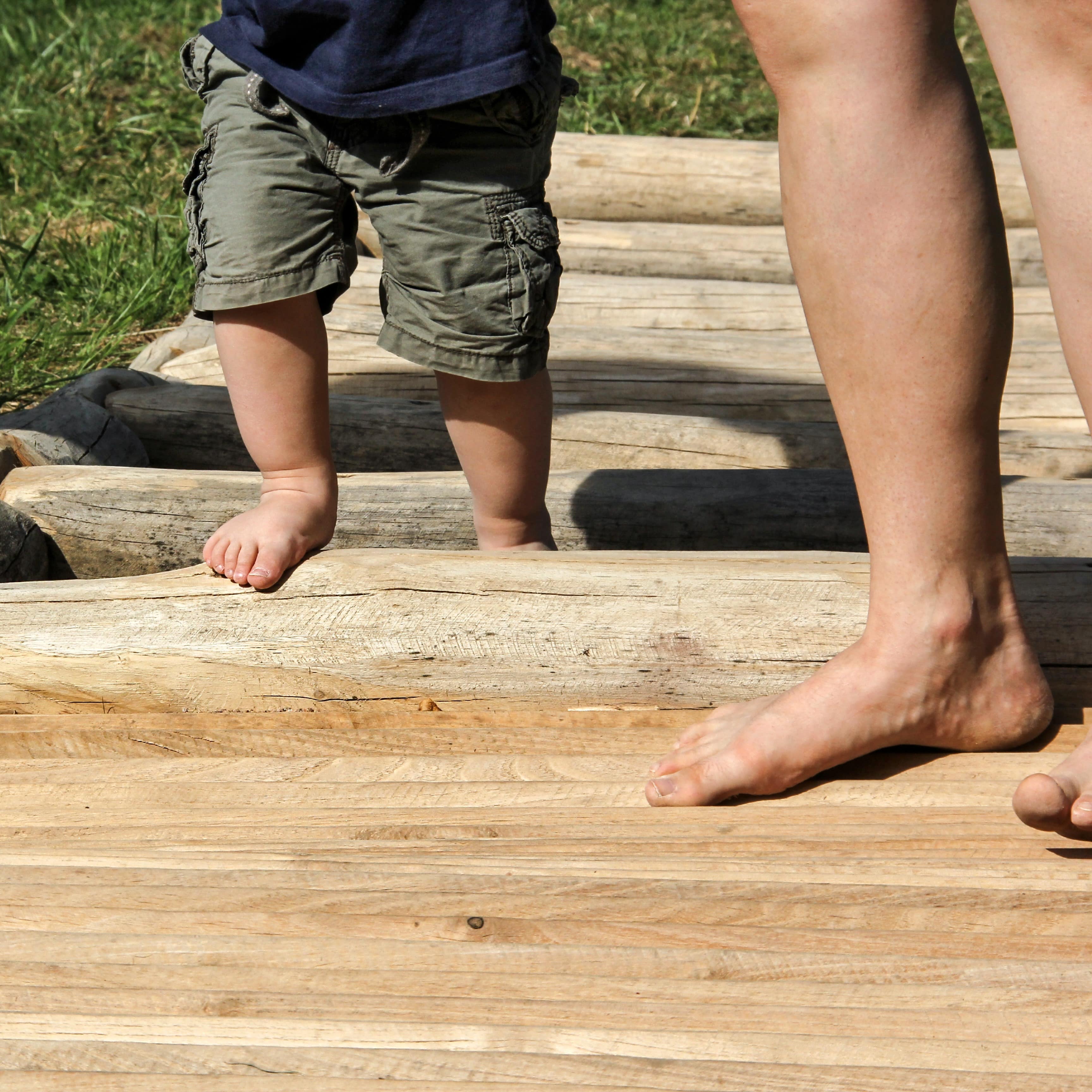 Beine einer Frau und einem Kleinkind auf einem Holzelement in einem Barfußpfad.