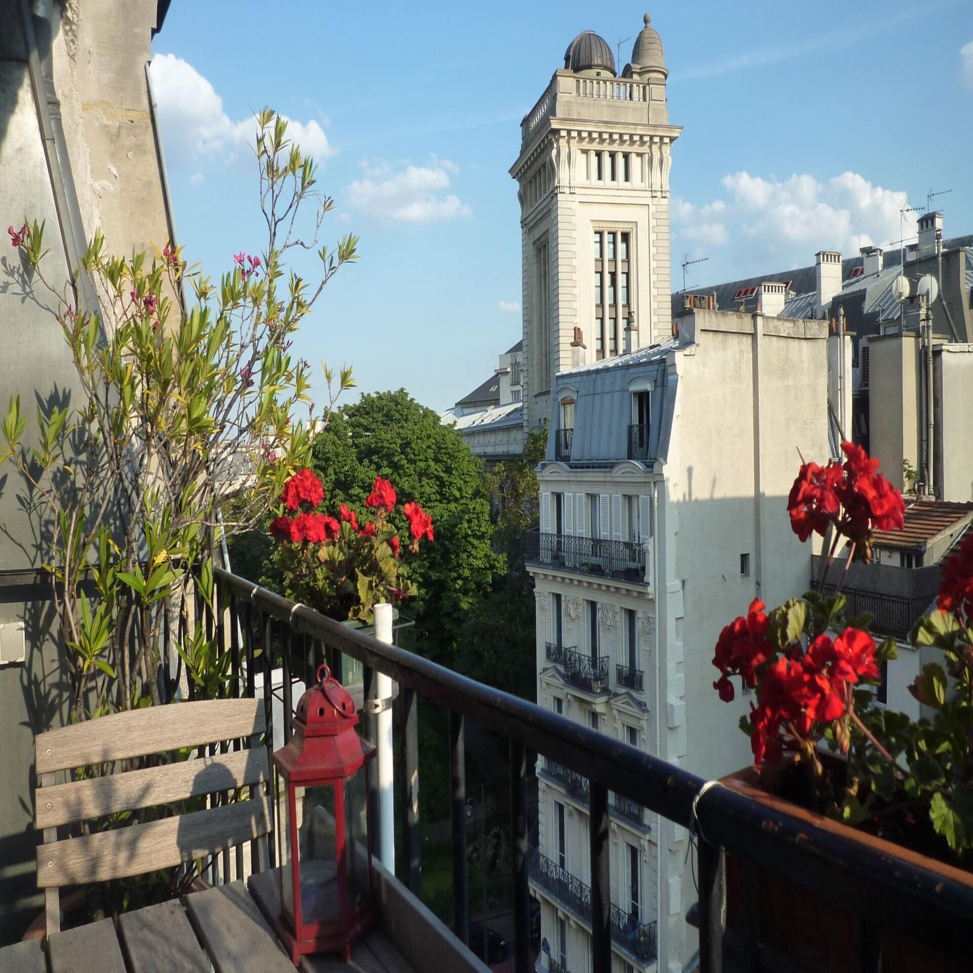 Blick von einem Balkon mit roten Blumen auf das sonnige Paris um Notre Dame herum.