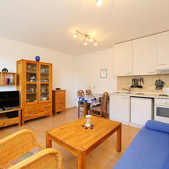 Die Wohnküche einer Ferienwohnung in Norddeich mit weißer Küche, blauem Sofa und hellbraunen Möbeln