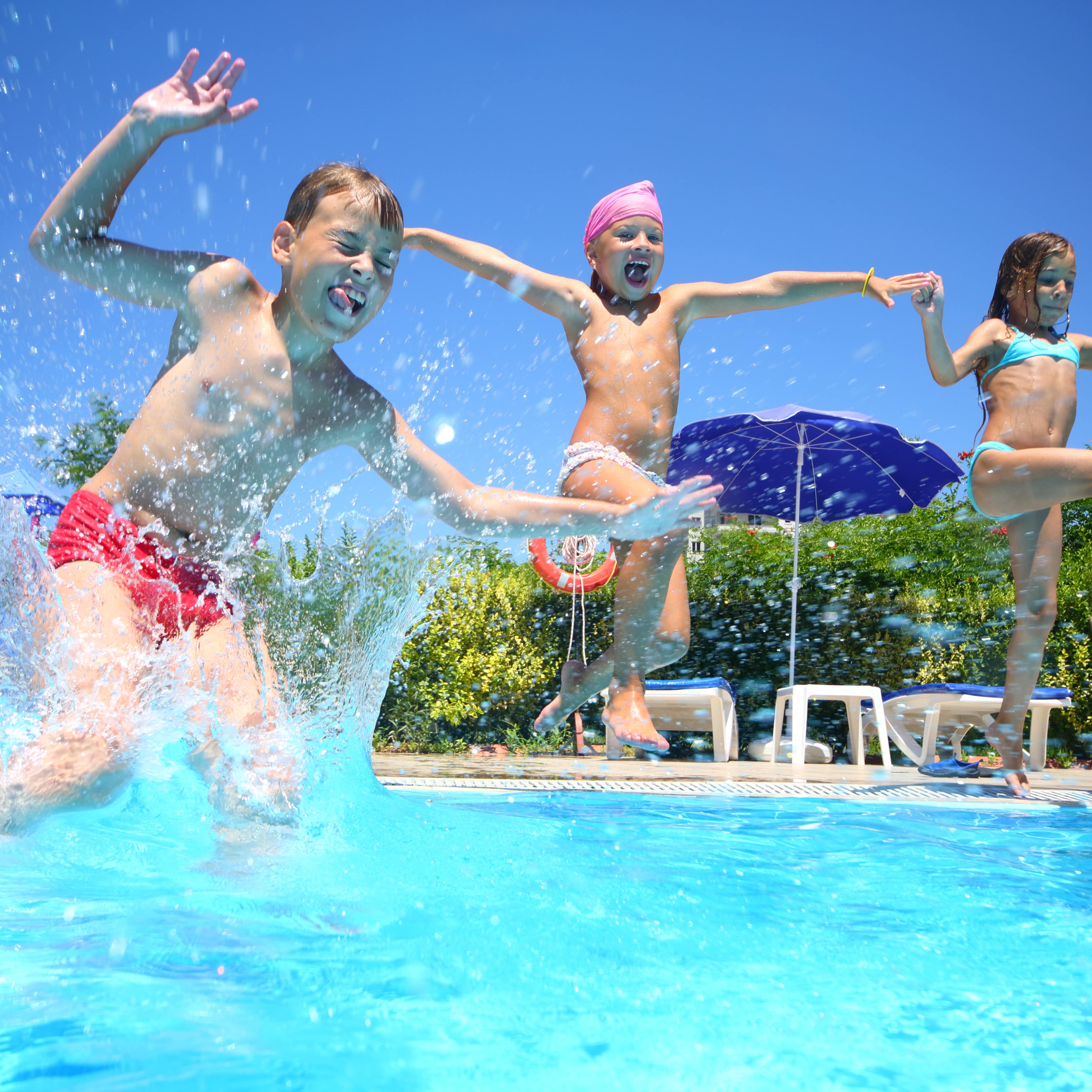 2 Mädchen und 1 Junge in Badebekleidung springen ins Wasser eines Freibads.