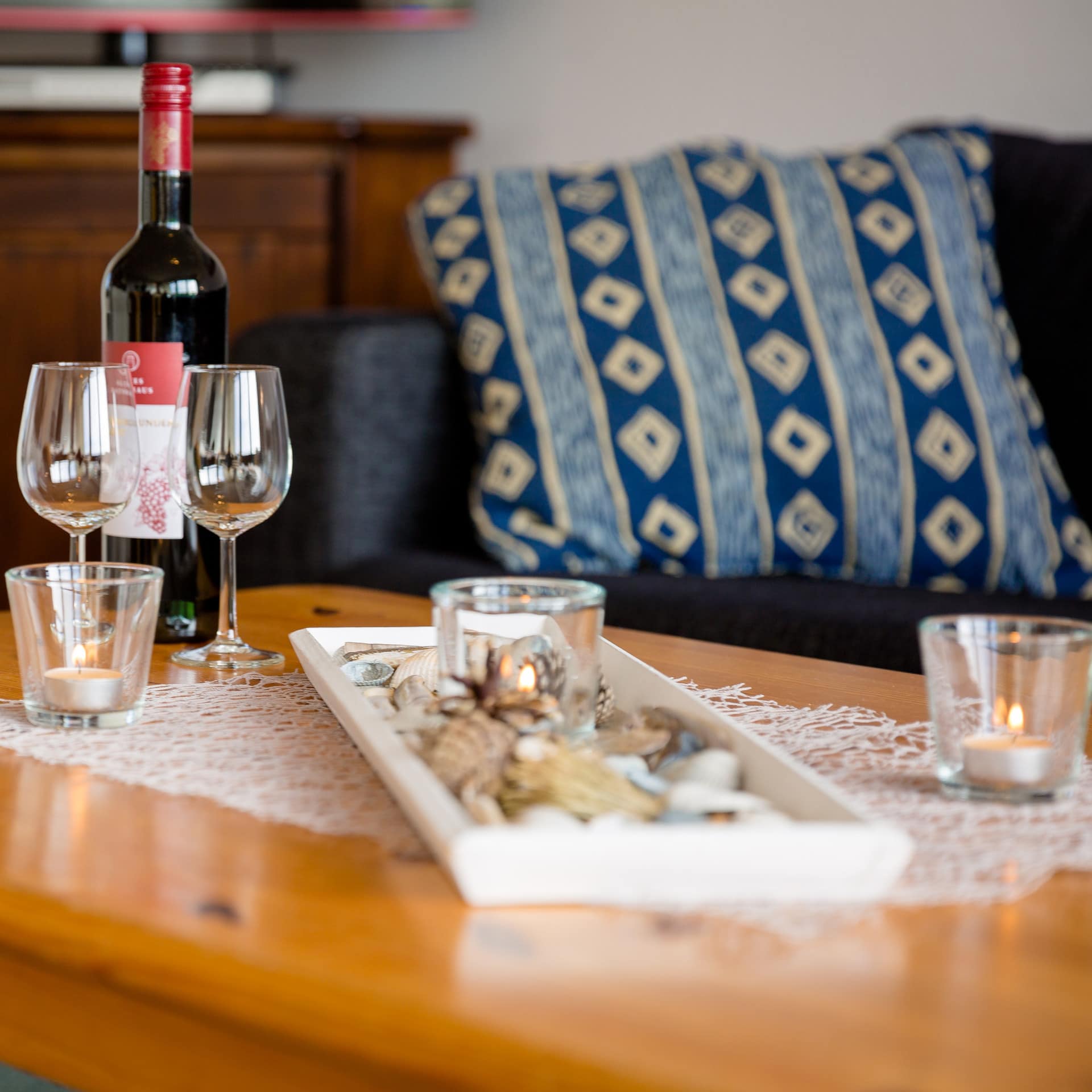 Ferienwohnung auf Ameland mit Sofa und Tisch, darauf eine Flasche Wein und zwei Gläser sowie Kerzen